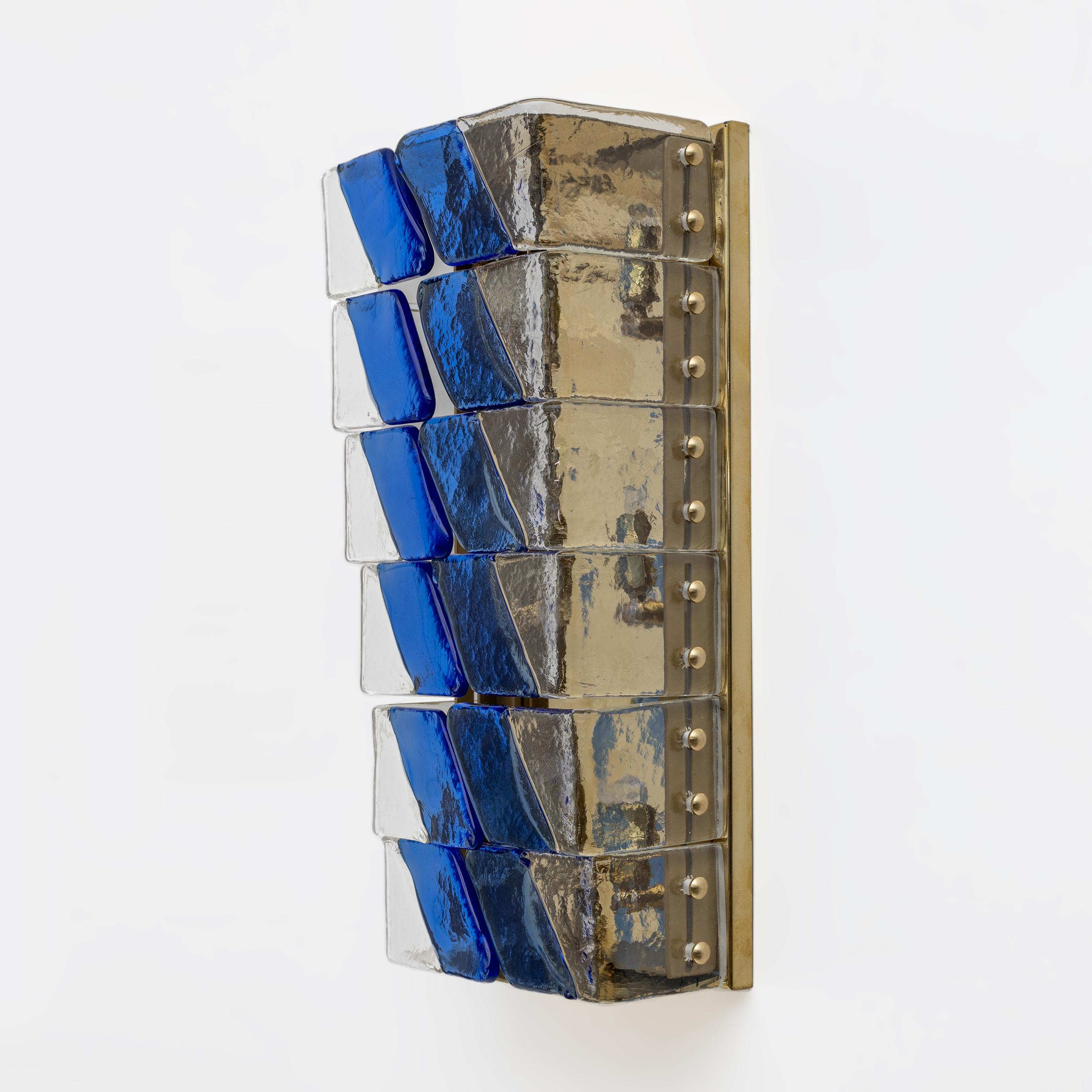 Questa coppia di lampade è composta da una serie di vetri di Murano sovrapposti in modo graduale. Gli occhiali hanno due tonalità di colore, chiaro e blu, che creano un effetto gradiente dinamico e visivamente accattivante. Sono montati su una