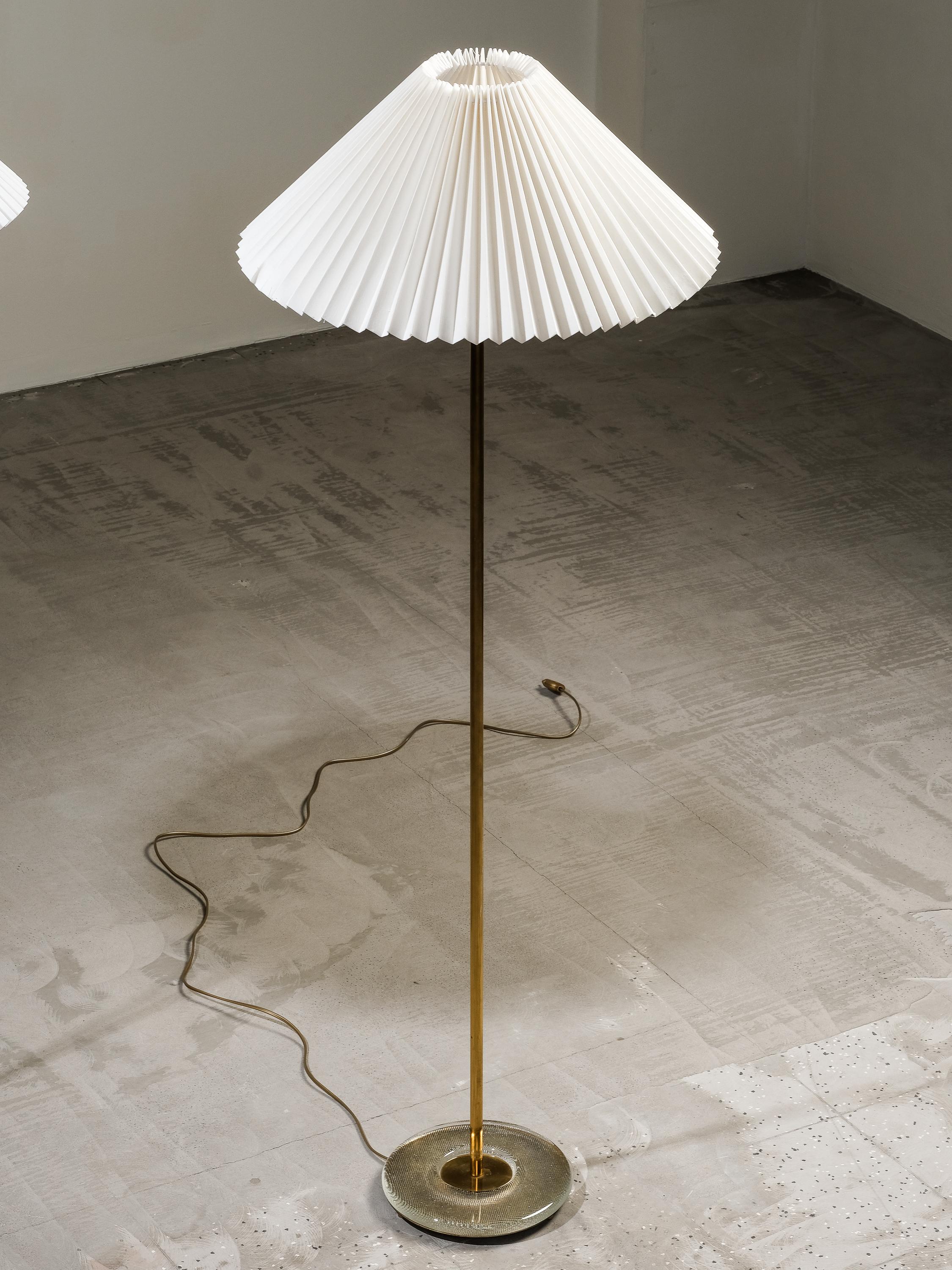 This elegant pair of floor lamps were manufactured in Sweden in the 1960s. The design is composed of a slightly raised, circular foot in textured glass. The central tubular stem is made of polished brass.

The lamps are marked with the