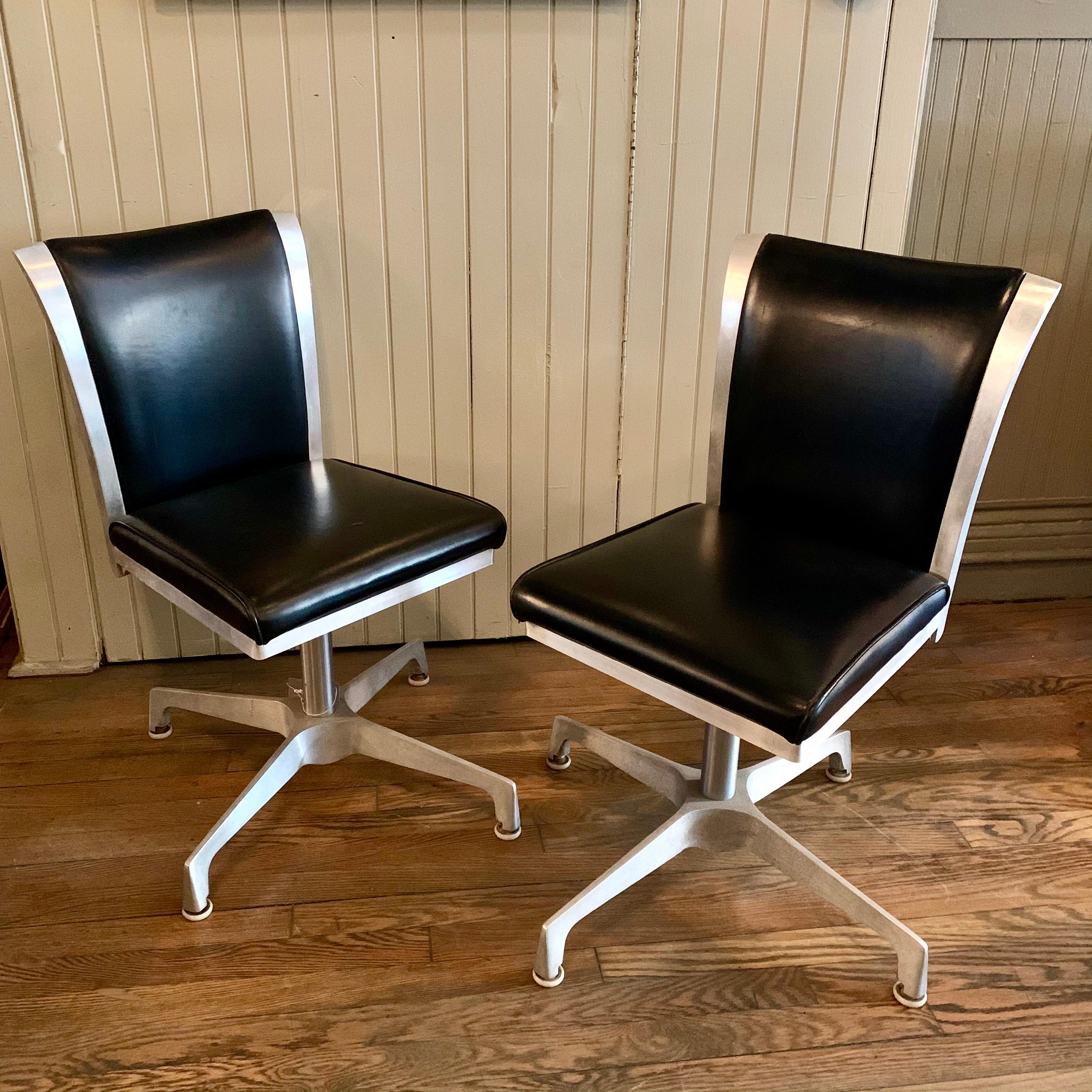 Pair of atomic, retro, Mid-Century Modern, swivel chairs fearure an aluminum trimmed frame with black vinyl upholstery.