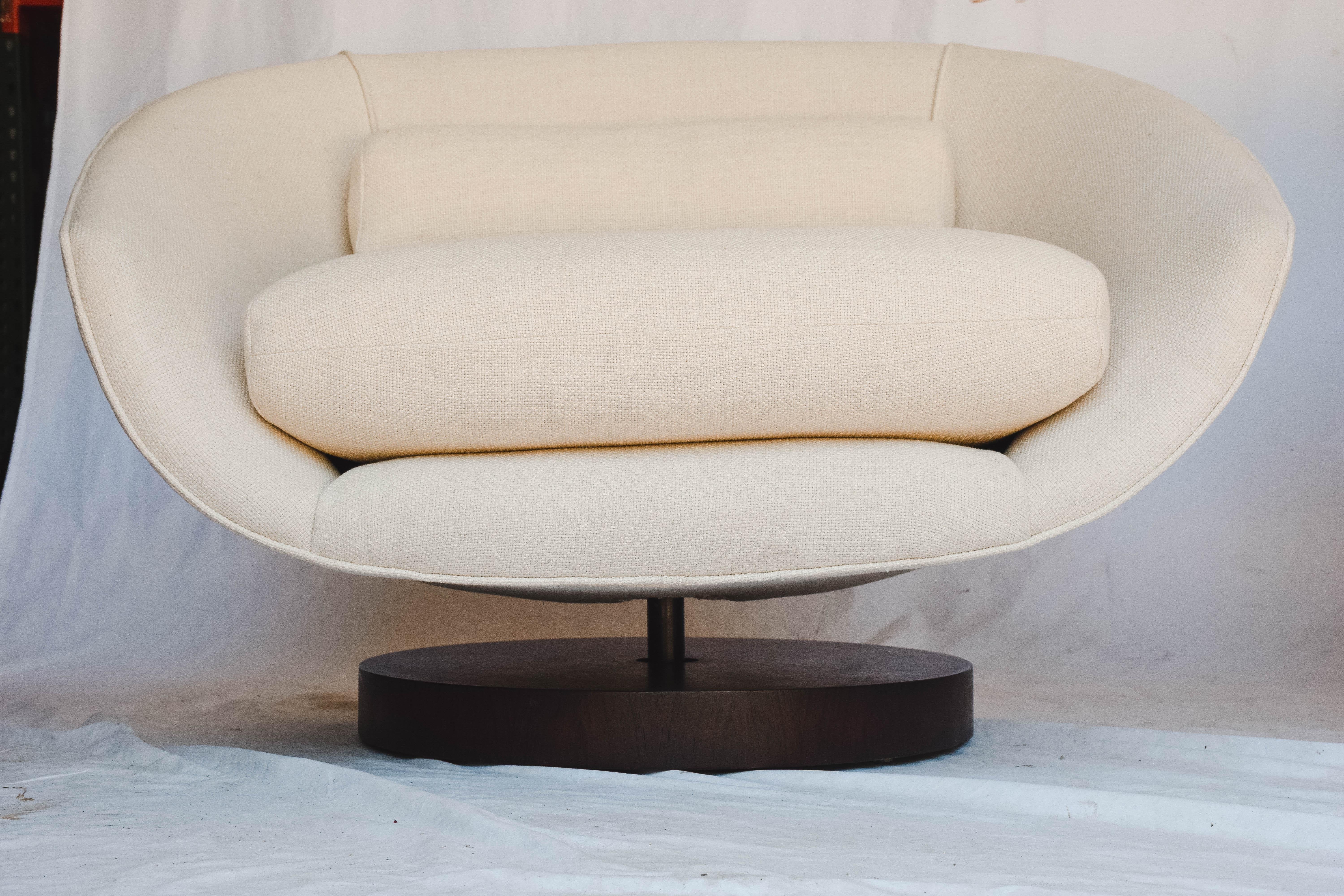 This beautiful pair of Mid-Century Modern lounge chairs have the ability to swivel and tilt with a versatile round wood base in the style of Milo Baughman. The pair of chairs are newly upholstered in a linen blend fabric, and feature a removable
