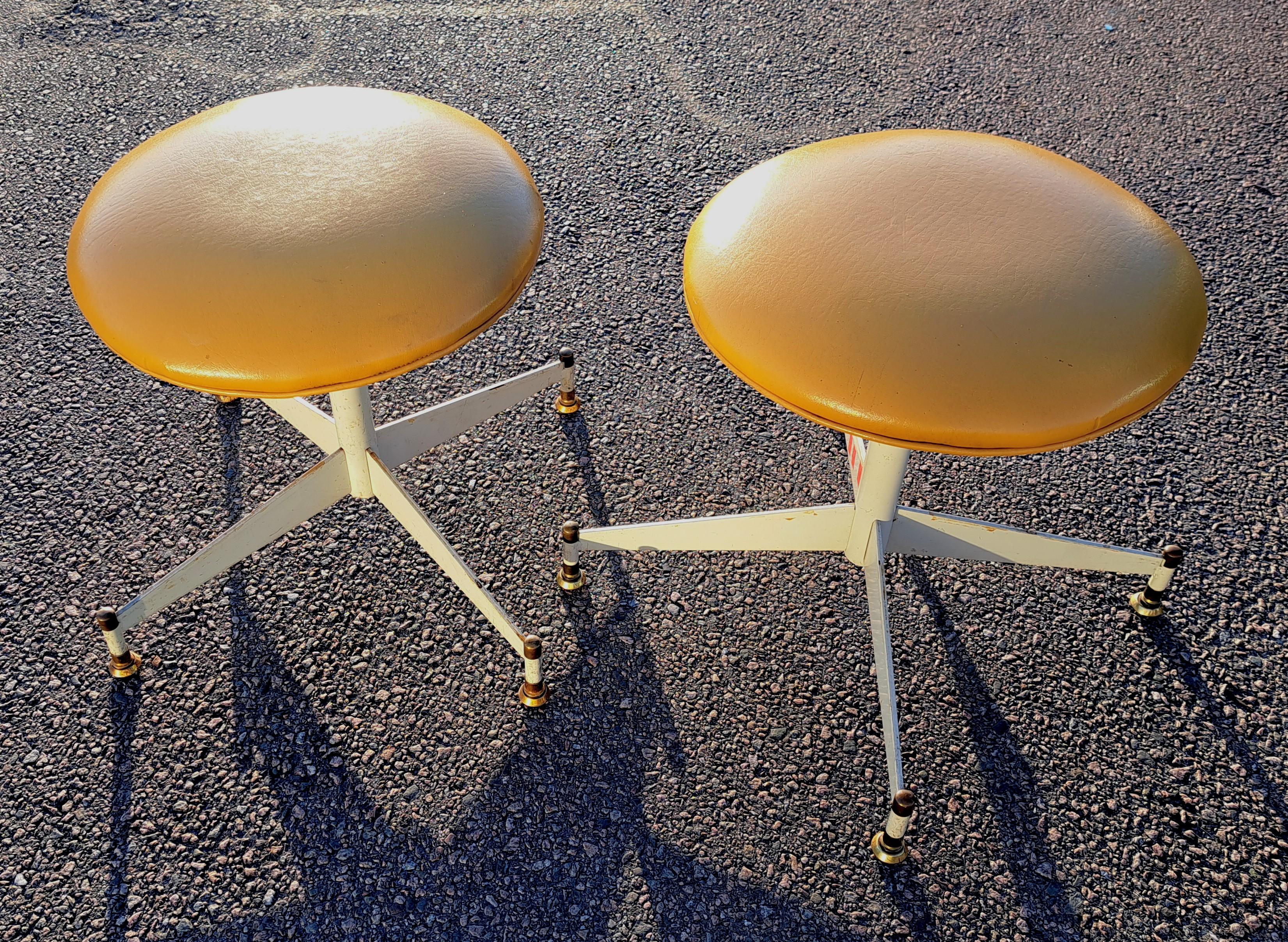 Pair of matching mid-century modern swivel footstools. Stools have a metal base with mid-century mustard colored vinyl seats.