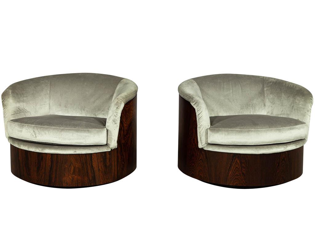 Pair of 1970s Mid-Century Modern swivel chairs by Plycraft. The chairs feature a swivel tub base and are encased in a rich wood exterior. They have been luxuriously upholstered in a slate designer velvet with a single seat cushion. A legendary chair