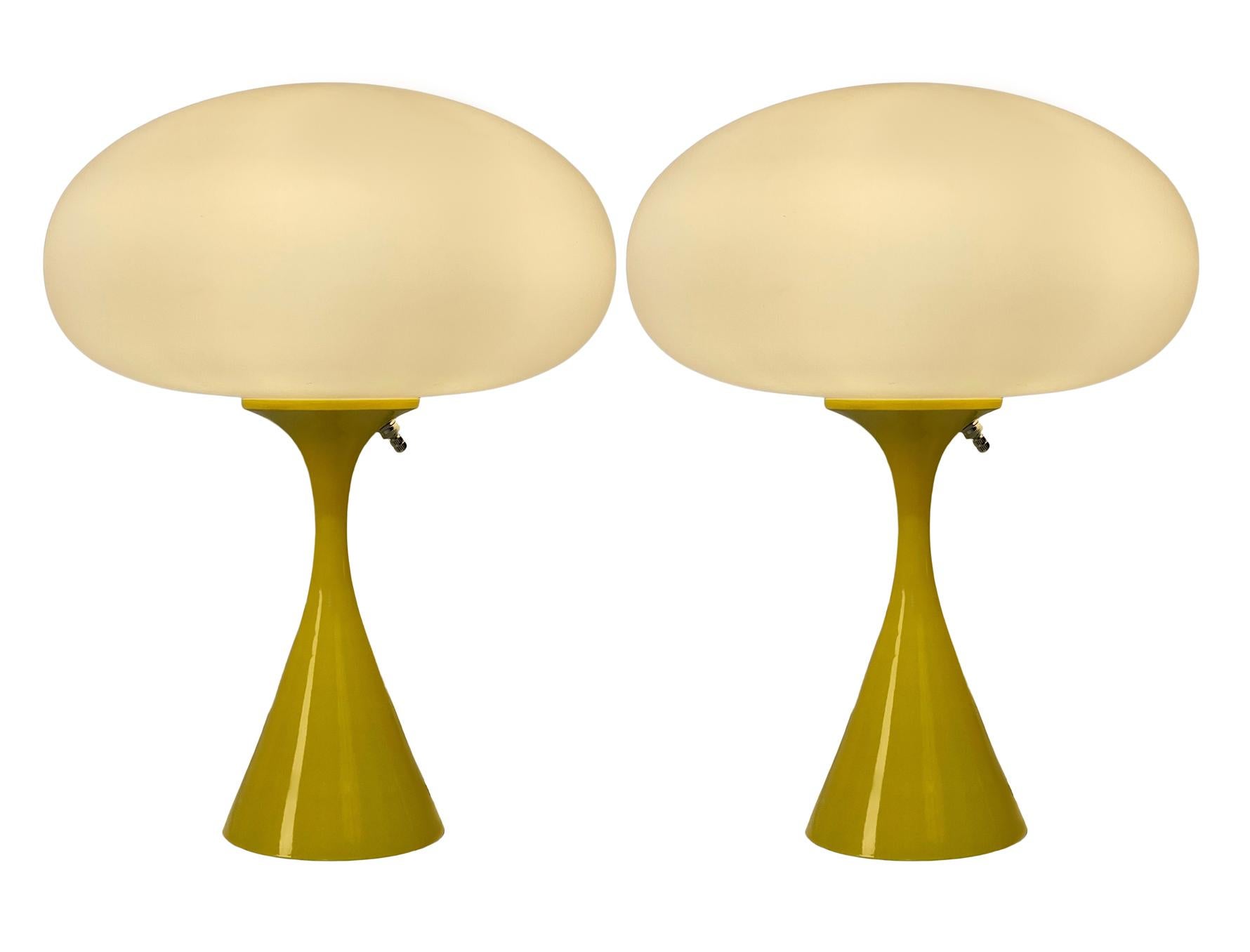 A handsome matching pair of table lamps in a conical mushroom form after Laurel Lamp Company. The lamp features a cast aluminum base with a yellow powder coat and a mouth blown frosted glass lamp shade. Price includes the pair as shown.