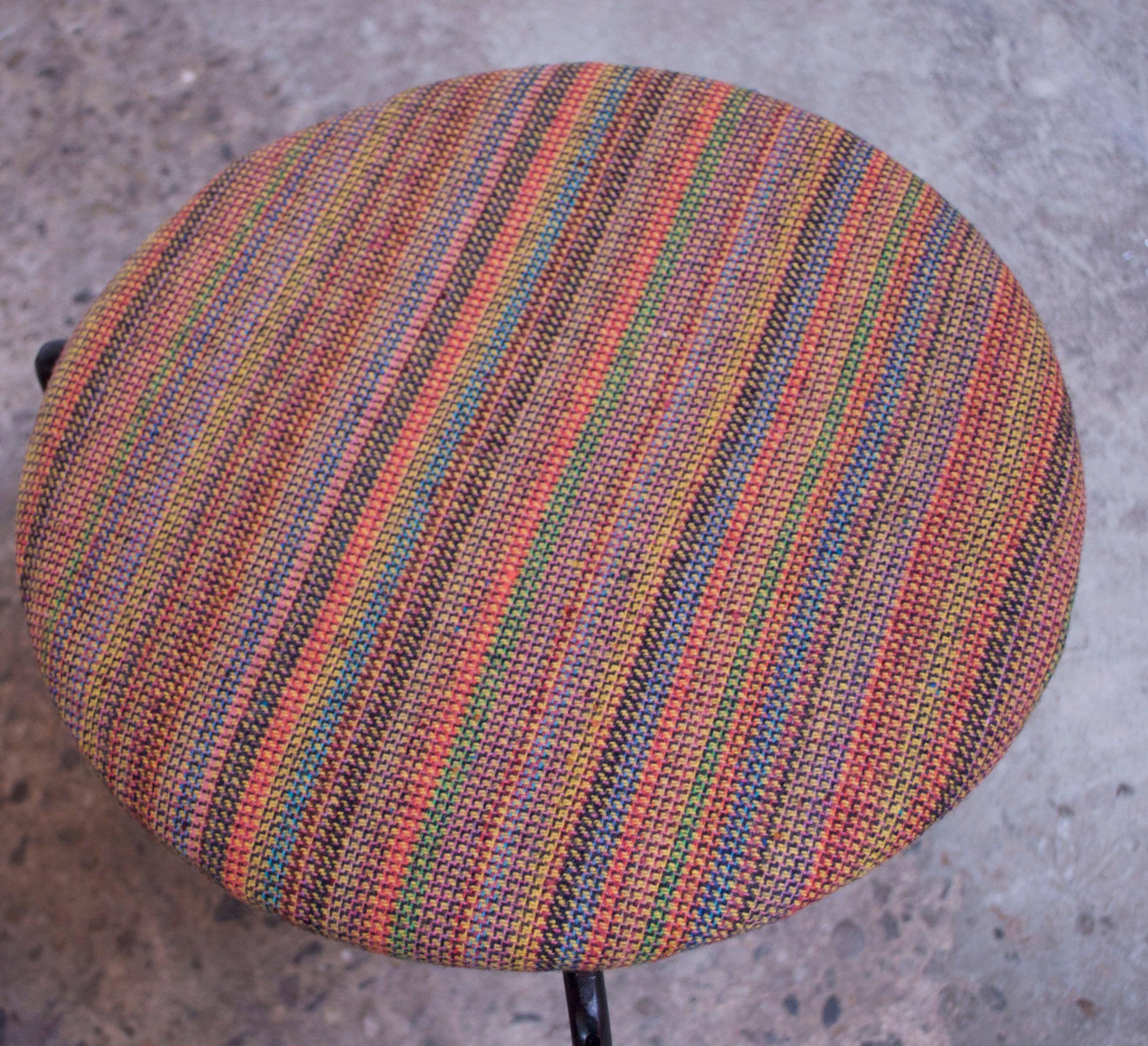 Pair of 3-legged low iron stools with oversized metal feet with gold-painted trim detail. Plywood seats have been reupholstered in a multi-color tweed fabric. Nice, vintage condition with only minor wear to the frames. Reminiscent of designs by both