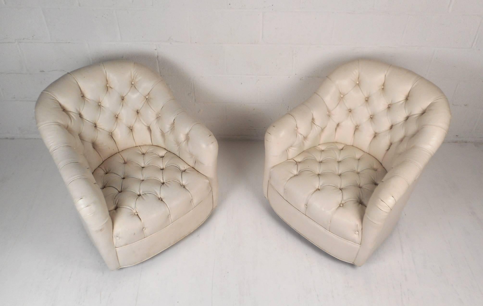 Stunning pair of vintage modern lounge chairs covered in white tufted vinyl. This wonderful pair has a comfortable barrel backrest with sloping arm rests. These stylish chairs have thick padded seating with deep tufts and wheels on the base ensuring