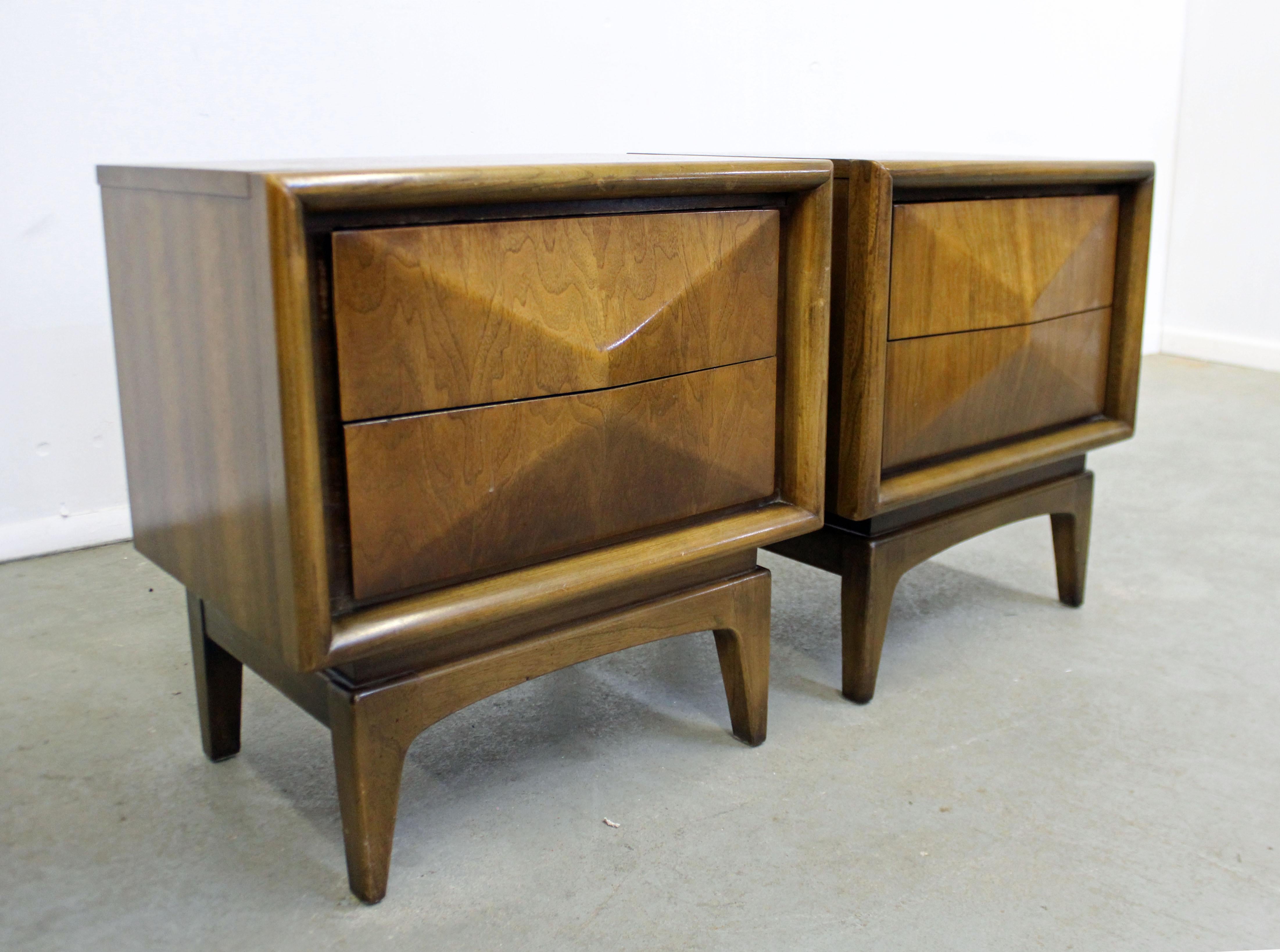 Offered is a pair of Mid-Century Modern nightstands made of walnut, each featuring a diamond style front with two dovetailed drawers and hidden side pulls. They are in good condition with slight surface scratches throughout. They are not signed, but