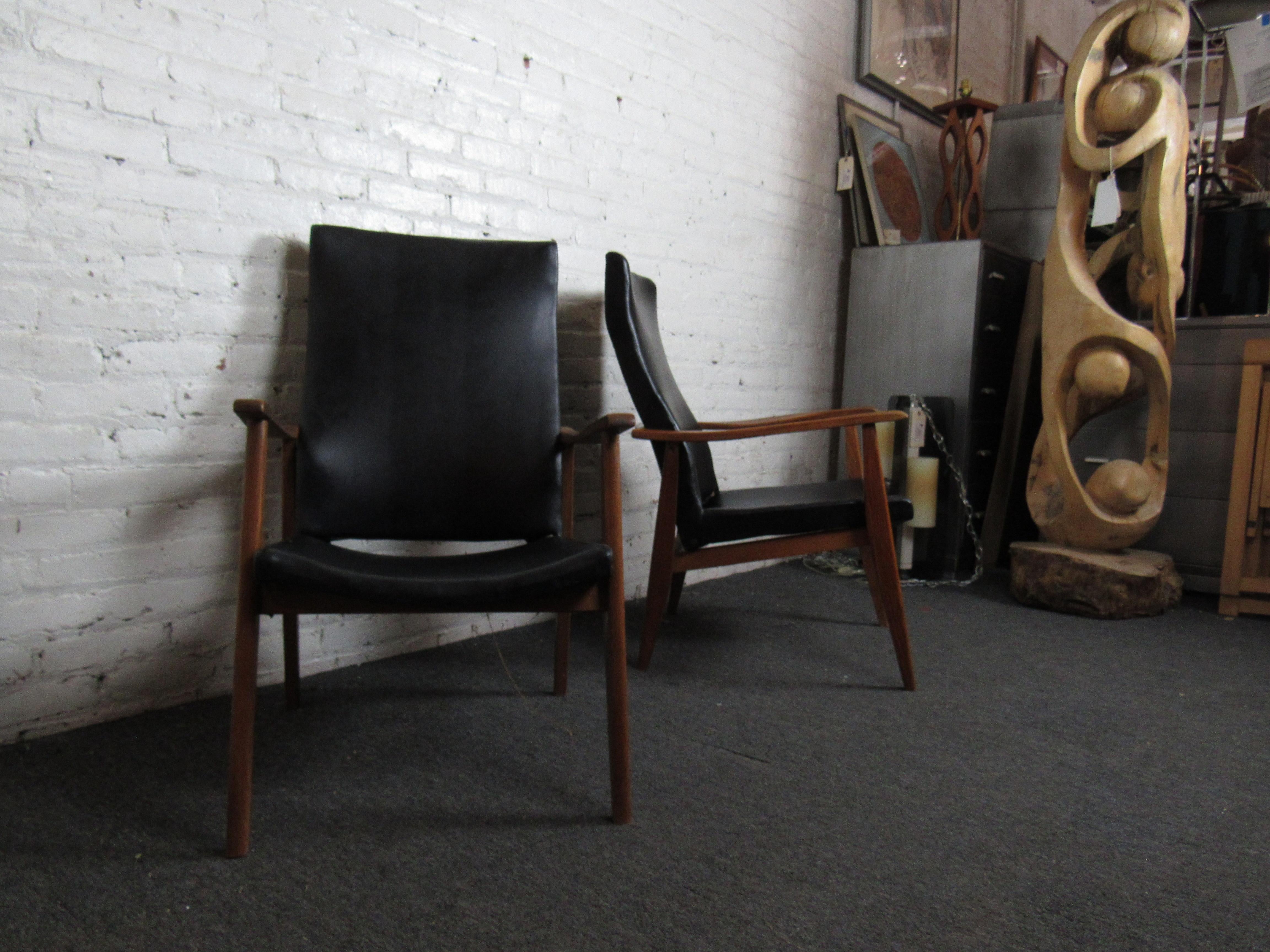 This vintage pair of Mid-Century Modern lounge chairs combines black vinyl with a rich wooden frame for a stylish and comfortable design. Please confirm item location with seller (NY/NJ).