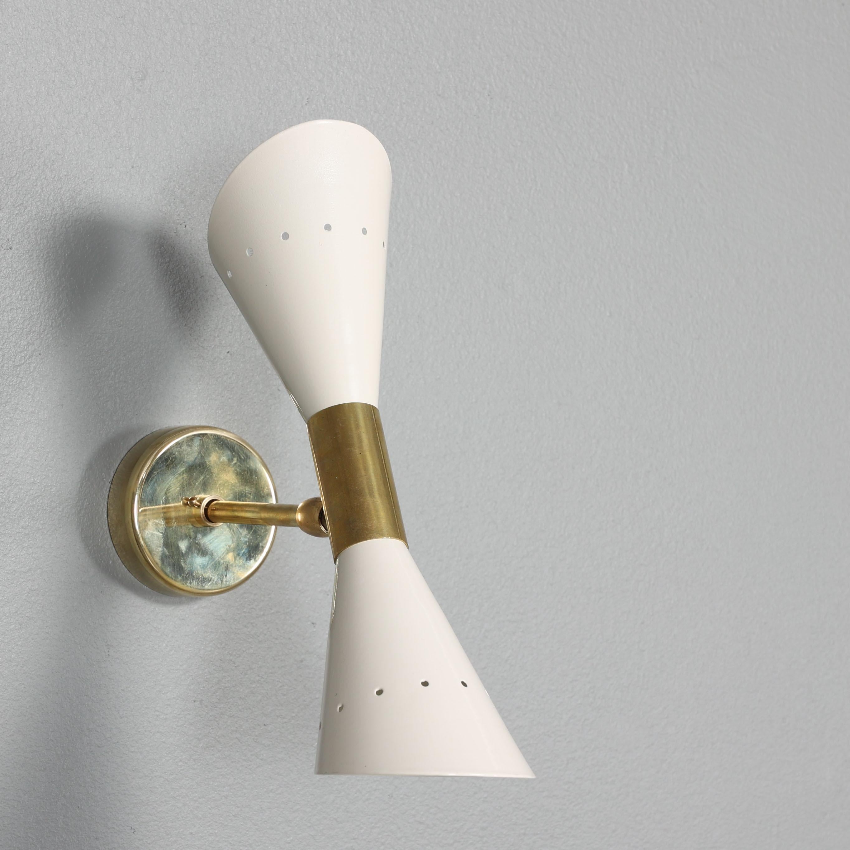 Un escultural par de apliques de pared de mediados de siglo, con una refinada interacción de latón pulido o patinado y metal lacado en marfil. Cada aplique está diseñado con una pantalla de doble cono y dos fuentes de luz, que ofrecen iluminación