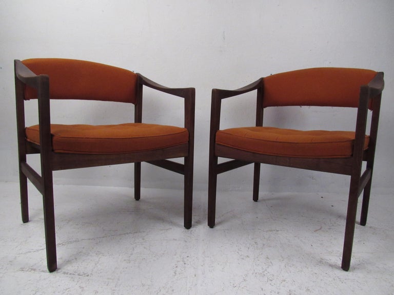 This stunning pair of vintage modern armchairs feature sloped armrests and orange tufted upholstery. A sleek and simple design that looks great in any modern interior. The sturdy walnut frame with stretchers on each side shows true quality