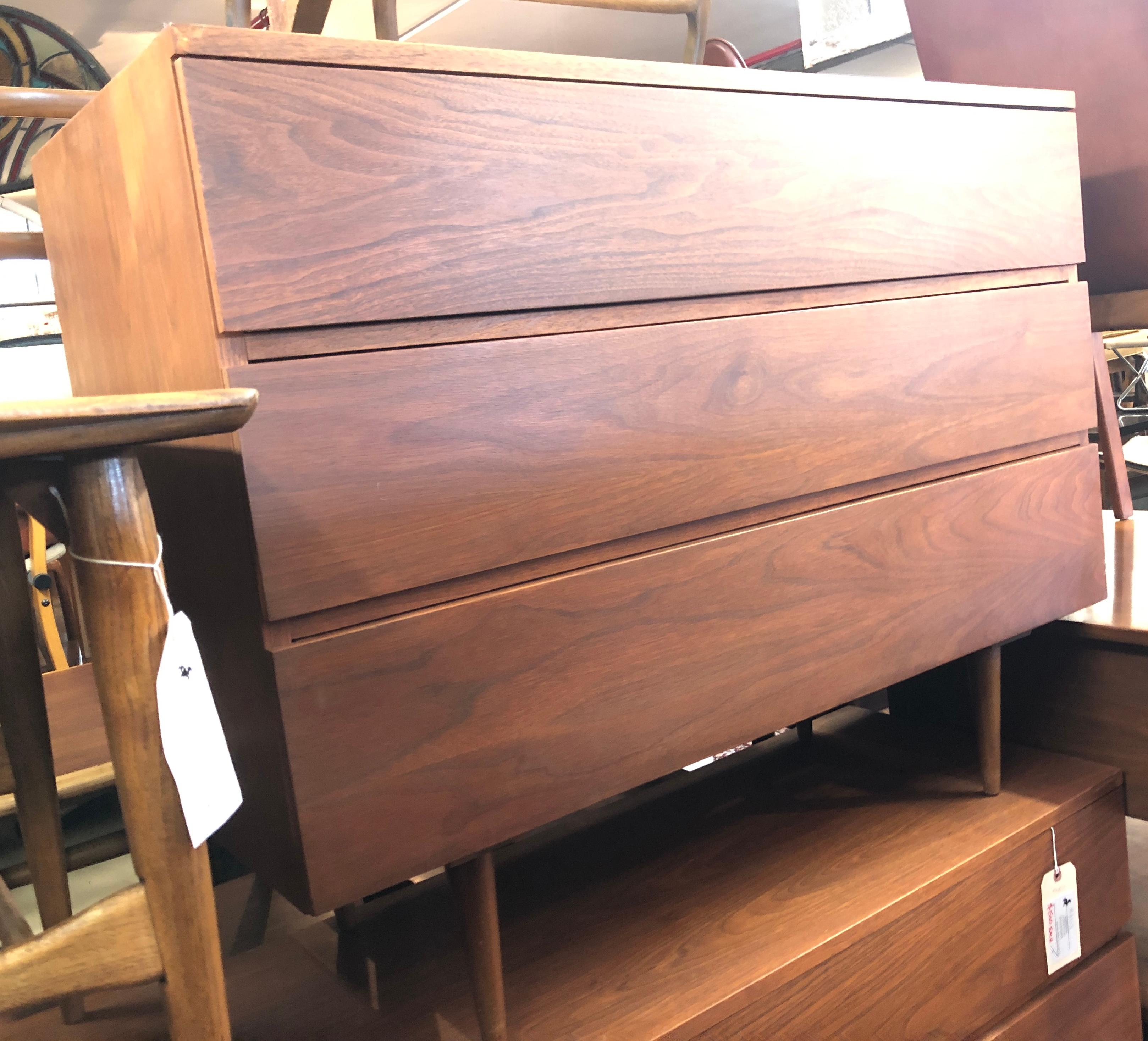 Cette magnifique paire de commodes modernes vintage dispose de trois tiroirs garantissant un grand espace de rangement. Design/One avec poignées de tiroirs cachées, finition noyer vintage et pieds fuselés. Cette paire est le complément idéal de tout
