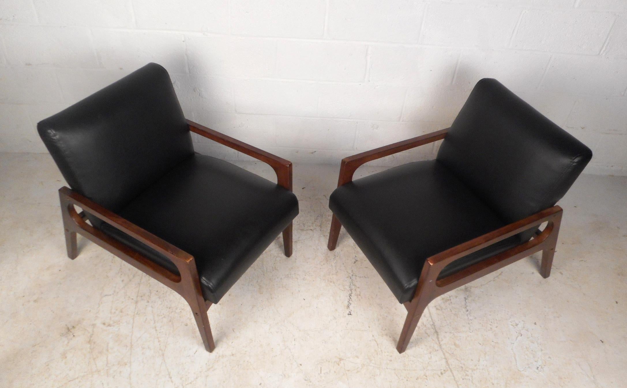 This stunning pair of vintage modern lounge chairs feature a sculpted walnut frame with low armrests and angled back legs. An extremely comfortable design with thick padded seating covered in black vinyl. This sleek and sturdy pair of midcentury