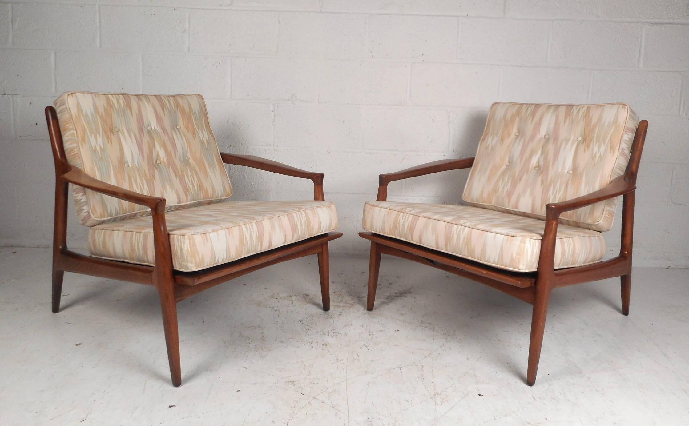 This wonderful pair of vintage modern lounge chairs feature an unusual cut out style back rest and sculpted arm rests. Well made chairs with a solid walnut frame and two overstuffed removable cushions covered in colorful upholstery. This comfortable