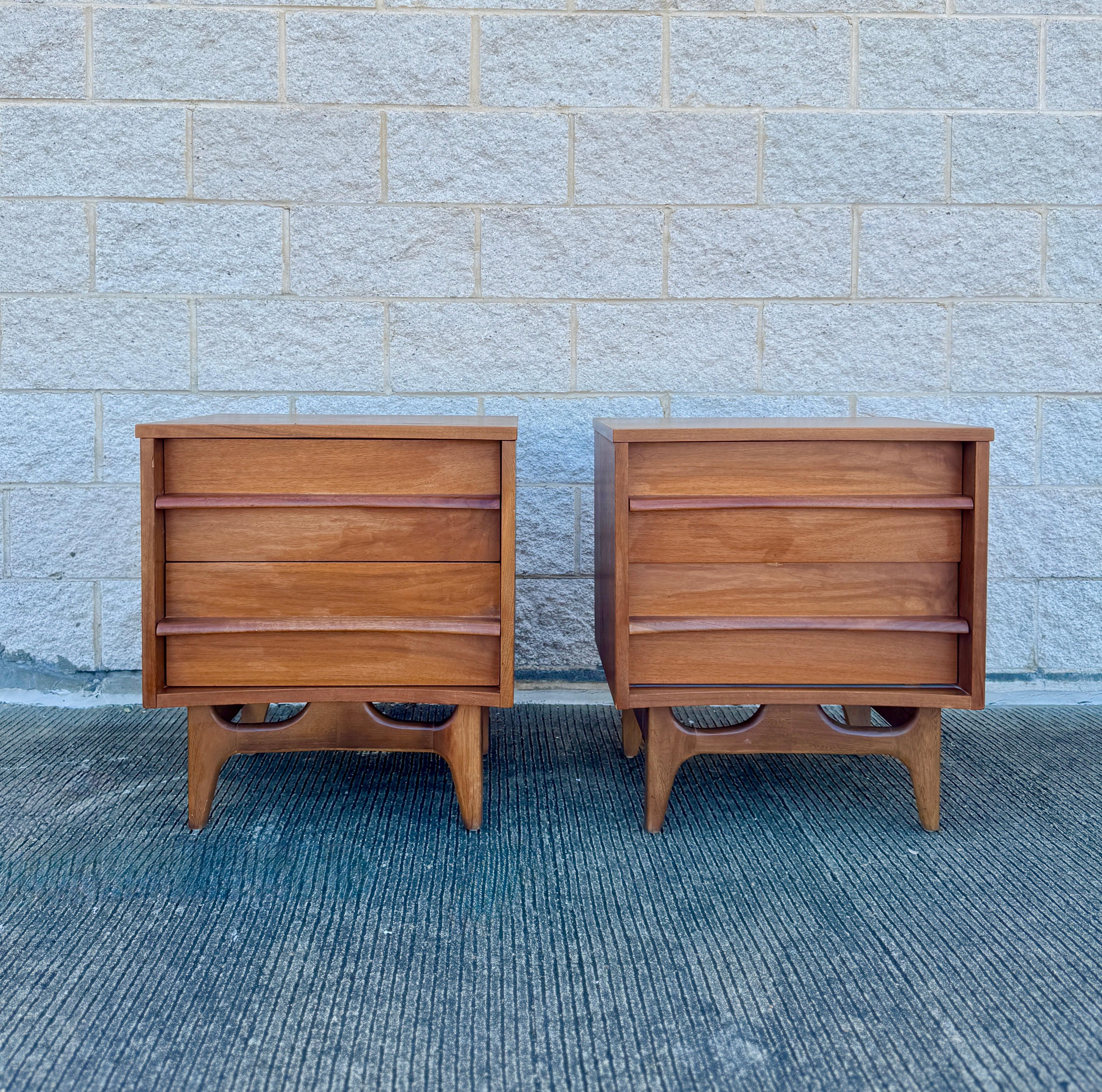 Una splendida coppia di comodini vintage in noce attribuiti a Young Furniture, risalenti agli anni '60. Questi pezzi classici del Mid-Century Modern sono caratterizzati da linee pulite, frontali dei cassetti scolpiti e basi con intagli ad arco. Ogni