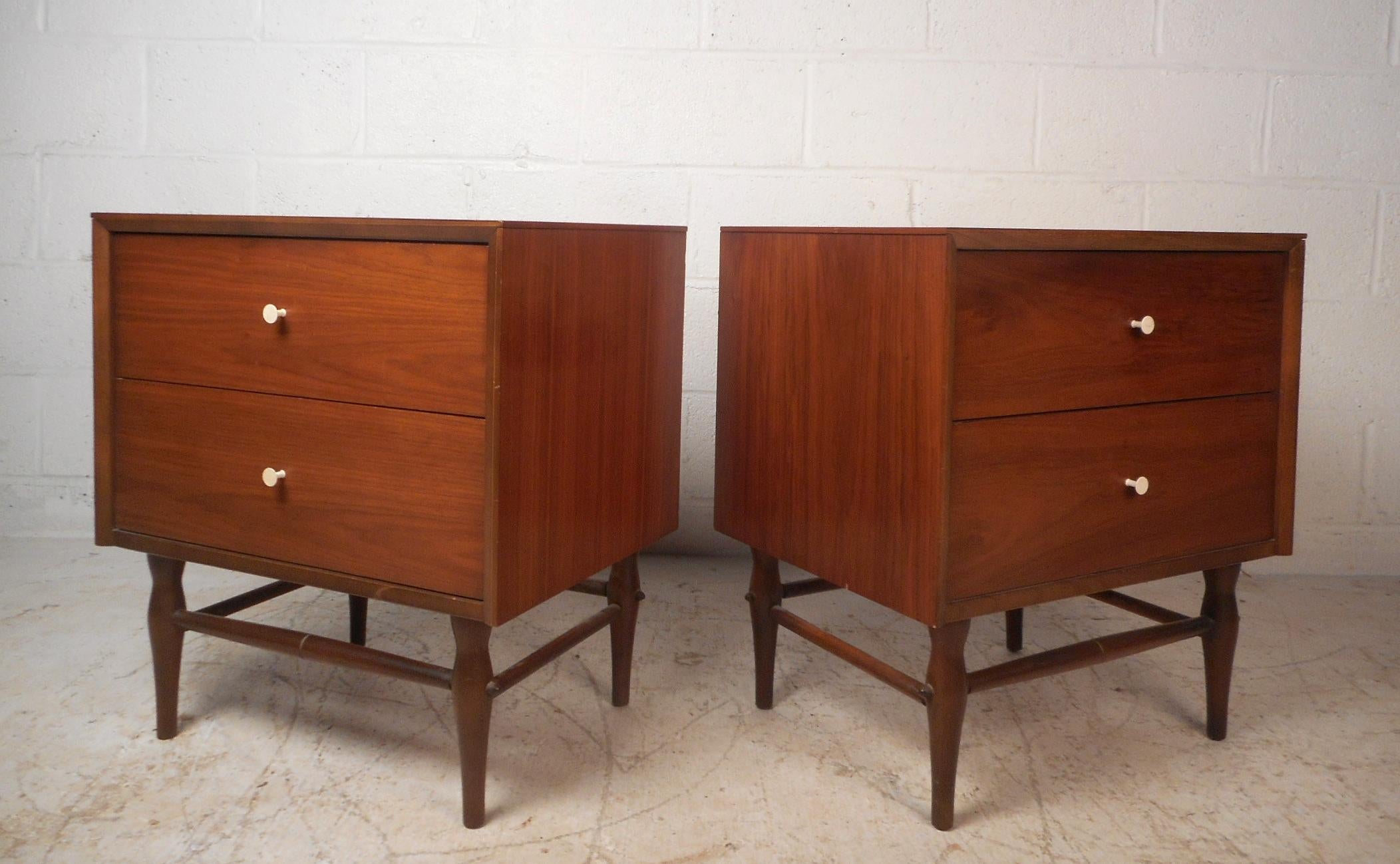 This stunning pair of vintage modern nightstands feature two large drawers with white circular pulls. The sleek design has sculpted and tapered legs with stretchers running all the way around. This stylish and sturdy pair of midcentury end tables