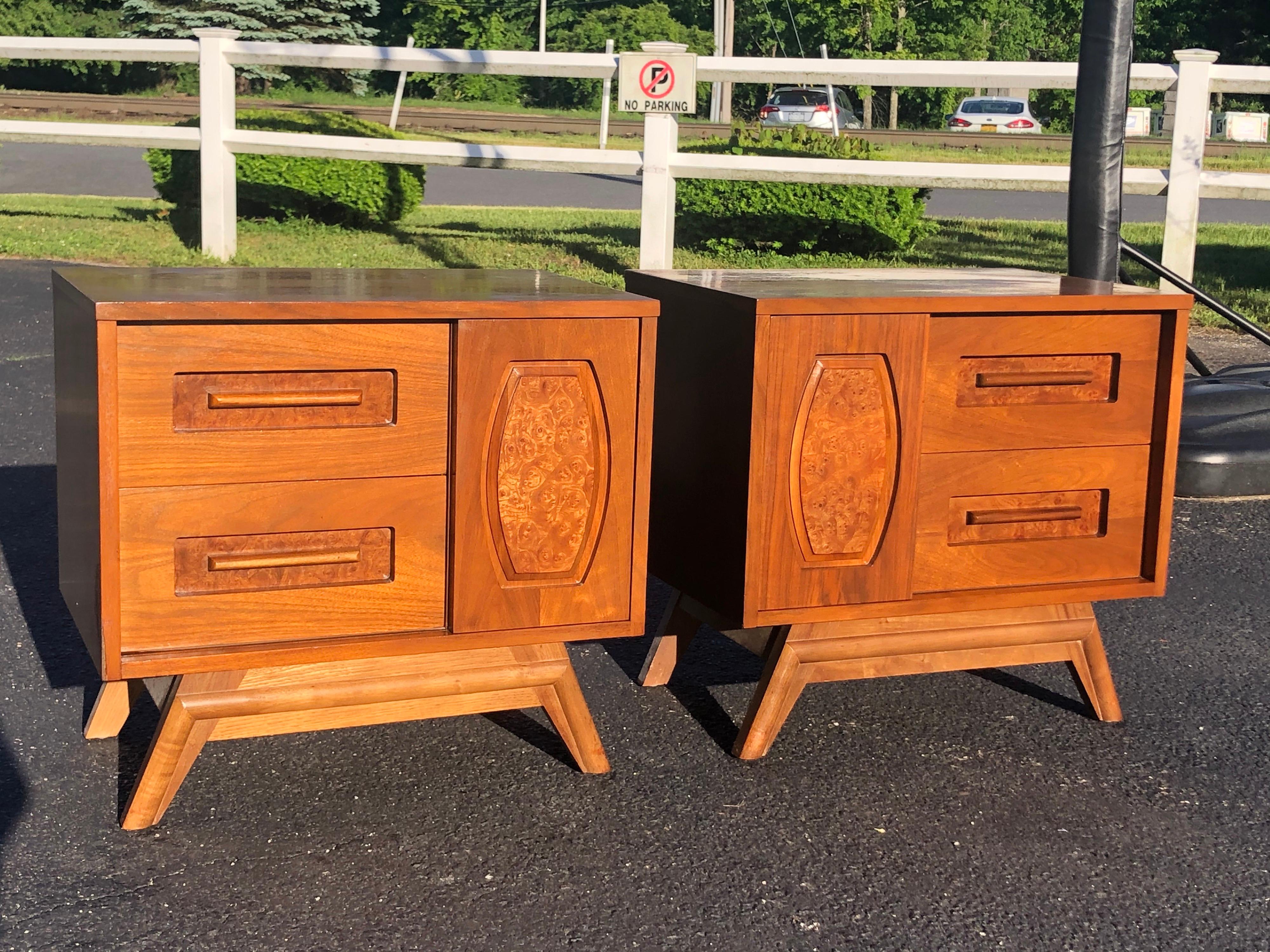 Pair of Mid-Century Modern walnut nightstands. Tiki style frontal design with one panel having burl wood inlay. Two drawers on one side and then a sliding cabinet door to reveal inside storage. Solid and well built. Perfect for that midcentury home