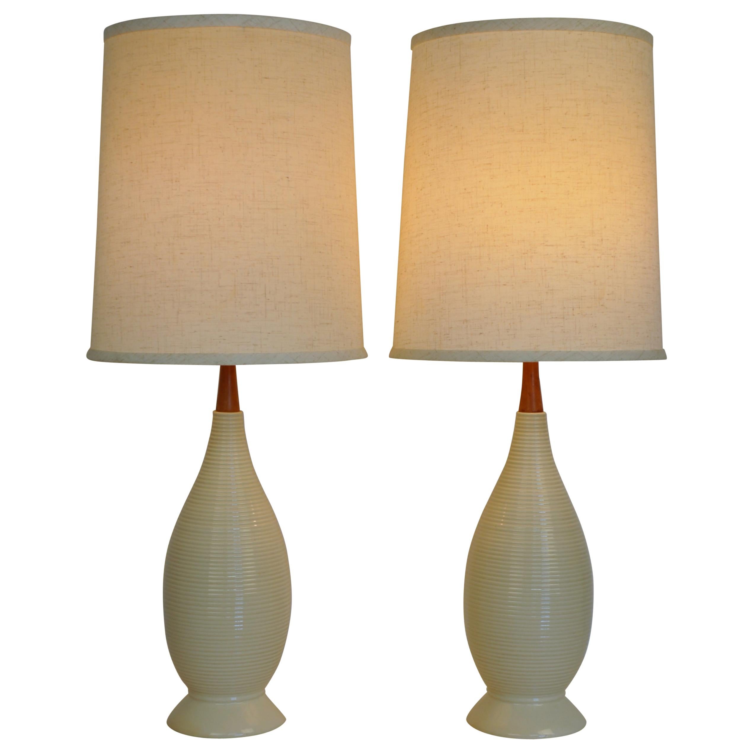A vintage pair of large Mid-Century Modern off-white ceramic and teak table lamps, dating from the 1950s. Each earth tone lamp features a glazed cream body with ridges, a teak neck and a creamy white linen shade. Work well with all Scandinavian or