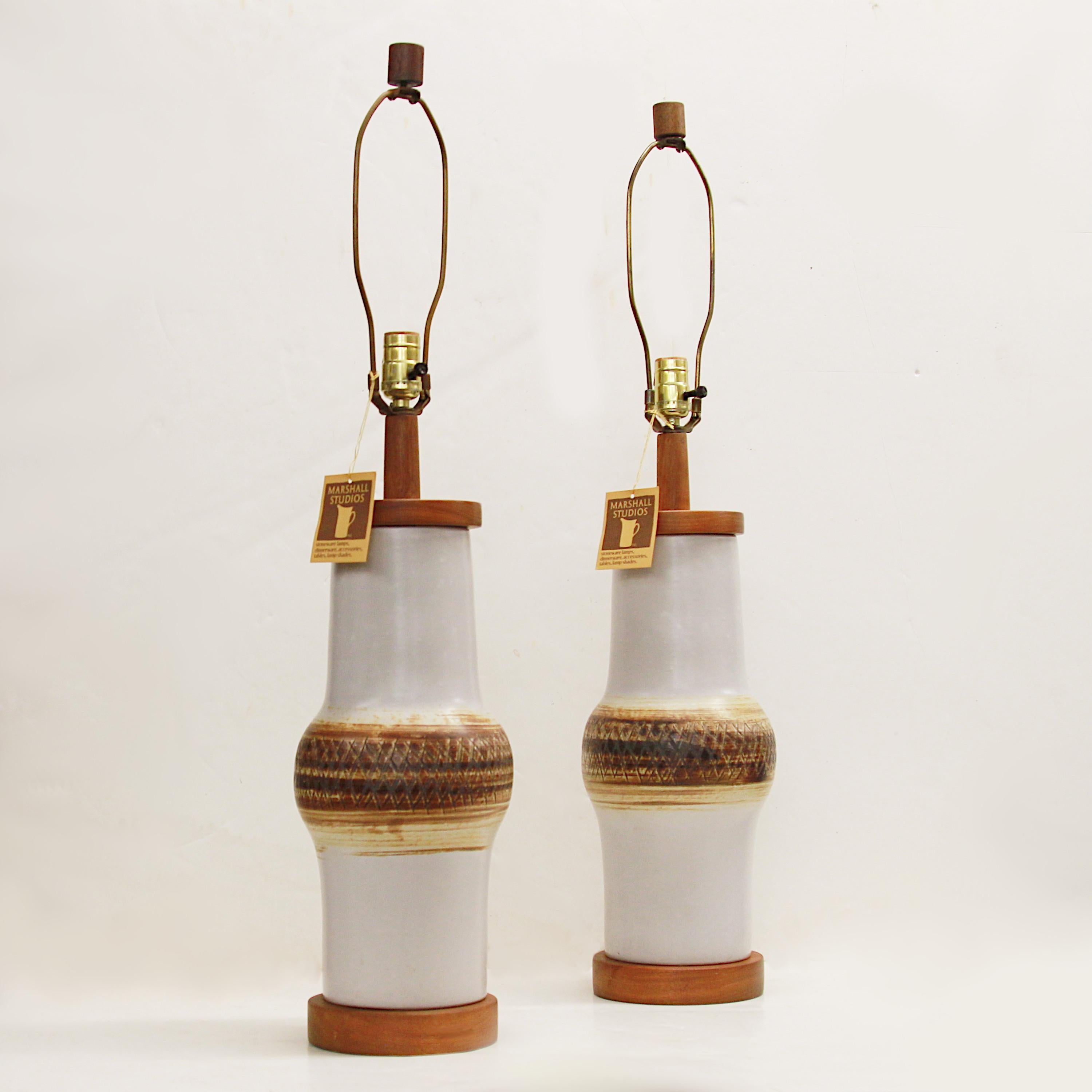 This wonderful pair of model 166-28-D65 table lamps were designed by Gordon & Jane Martz and manufactured at their Marshall Studios facility in Veedersburg, IN. Lamps features a matte white ceramic body with brown, incised design and turned walnut