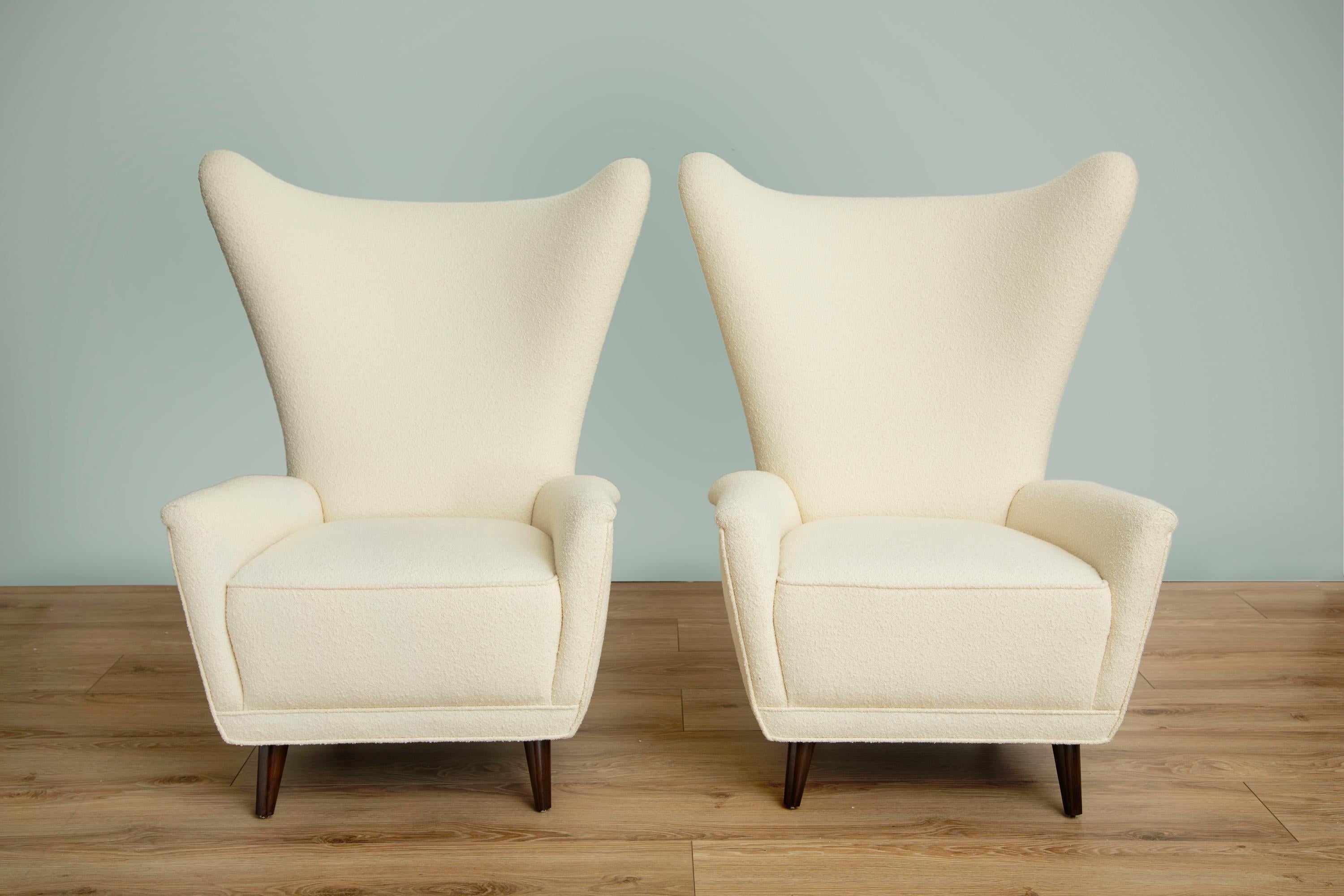 Pair of Mid-Century Modern wingback lounge chairs in the style of Gio Ponti,
High backrest with curvaceous wings and gently curved armrests,
Comfortable Classic lounge chair newly upholstered in pearl bouclé by Knoll,
Ebonized conical wood