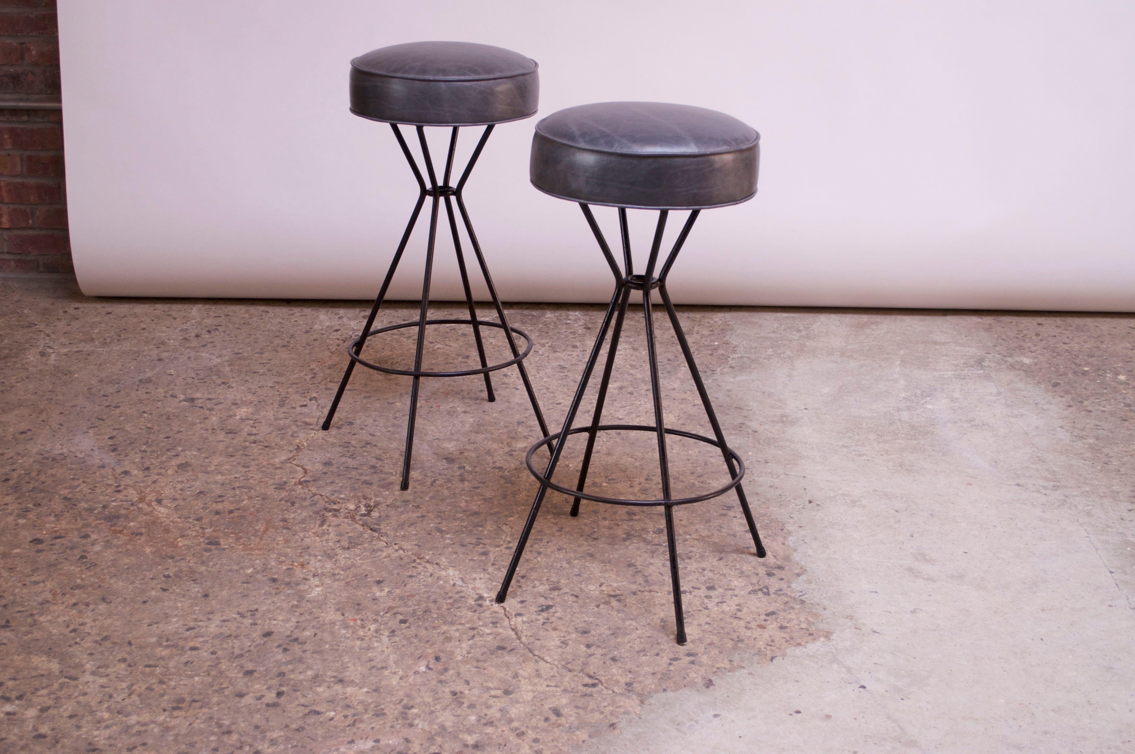 Pair of 1950s American modern bar stools composed of round, swivelling leather seats atop wrought iron bases with circular footrests. Distressed, gray leather and foam are new.
Measures: H 31.5