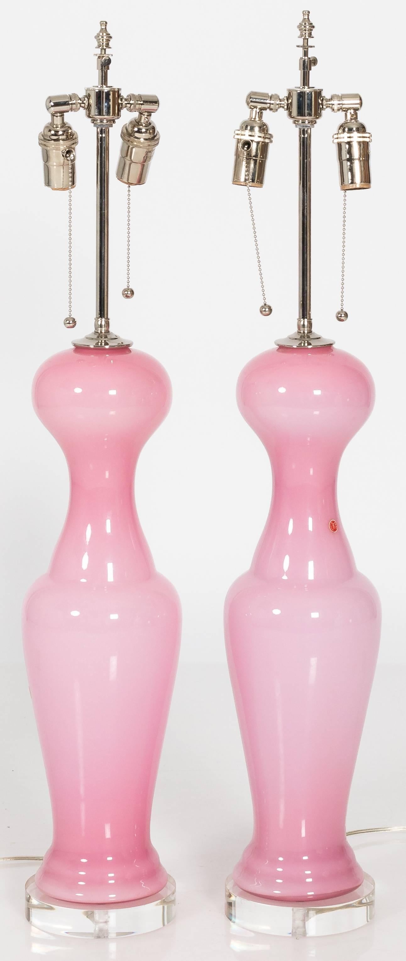 Pair of midcentury curvy light pink Murano glass lamps on new round Lucite bases. Light pink glass that is slightly translucent. Original red Murano stickers on each lamp. Newly rewired and in working condition. Each lamp uses two standard bulbs.