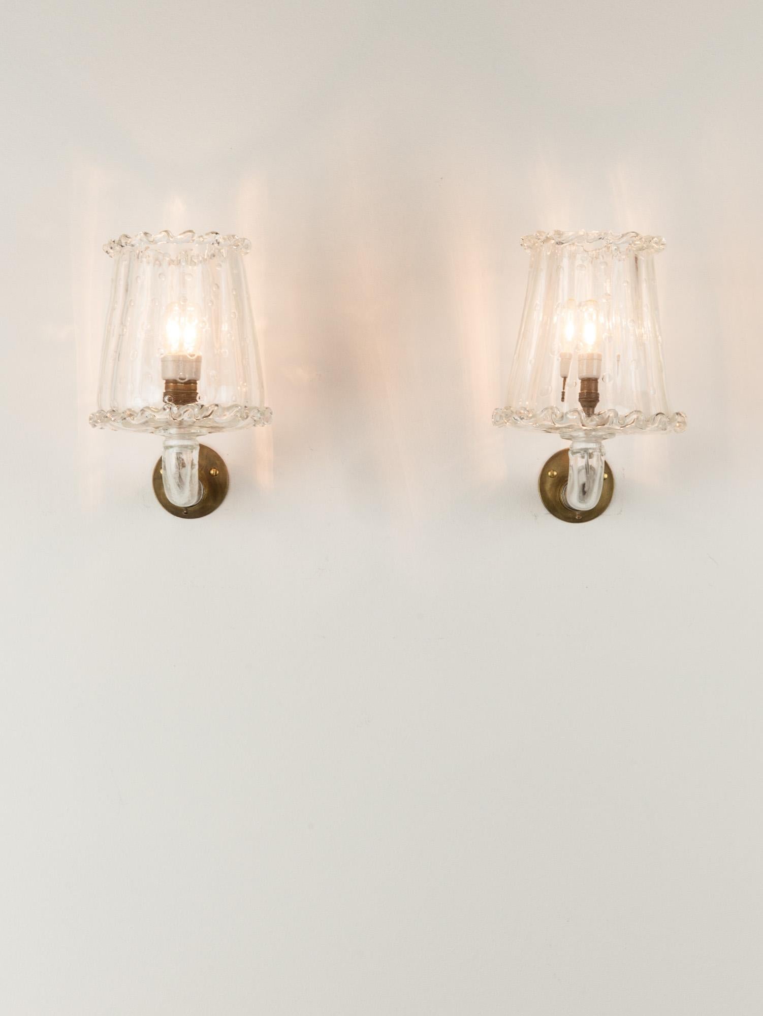 
Sweet and elegant pair of Italian Murano wall lights by Barovier with a ‘Bullicante’ glass shade and brass fixtures. The molded glass shade has lovely wavy detailing on its edges and a soft and delicate bubble texture. The curved stem is also made