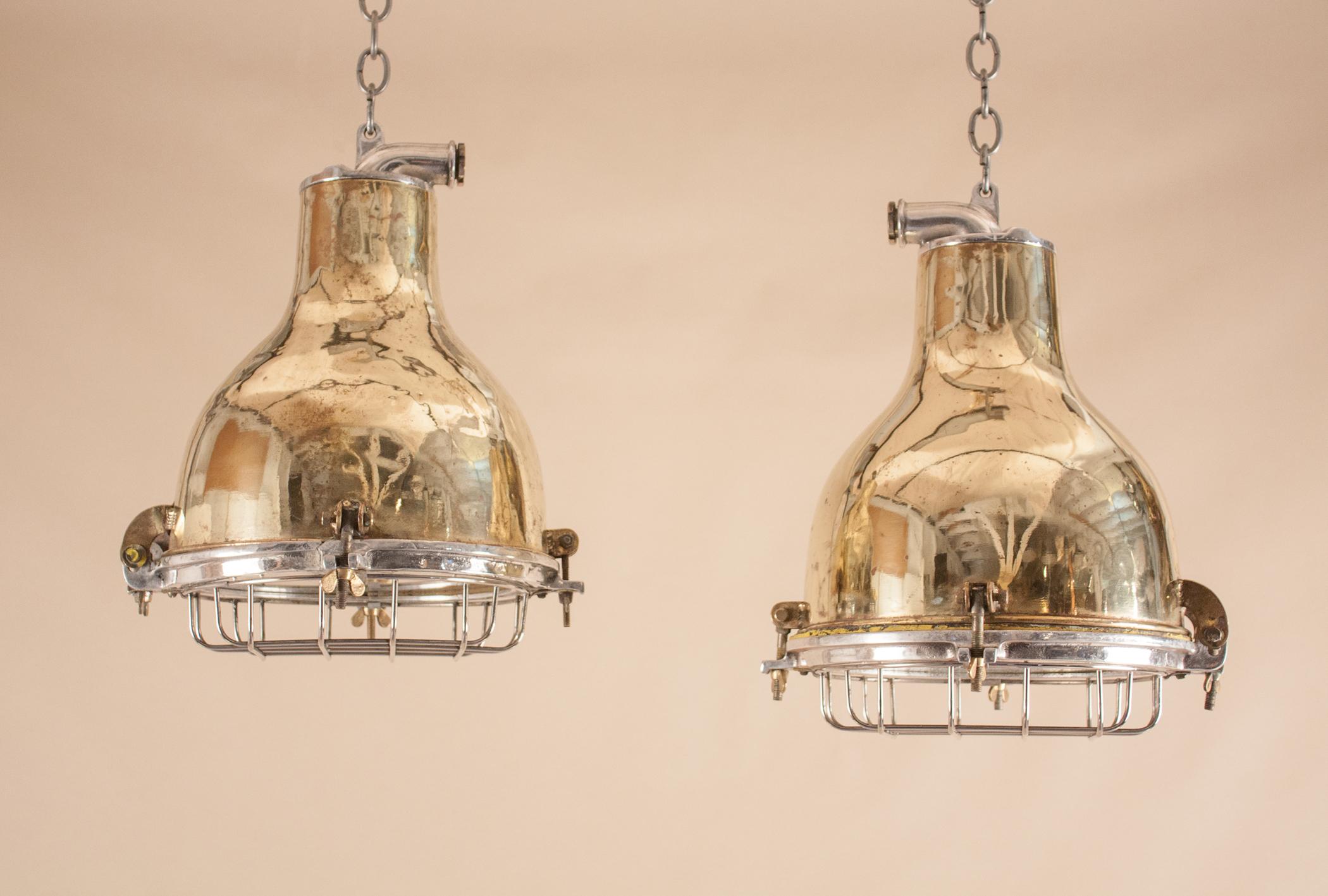 An attentively restored pair of industrial maritime pendants with an appealing brass patina and traces of original paint. Optional, and a matter of preference, these circa 1950 brass spotlights can be used with or without the protective cast