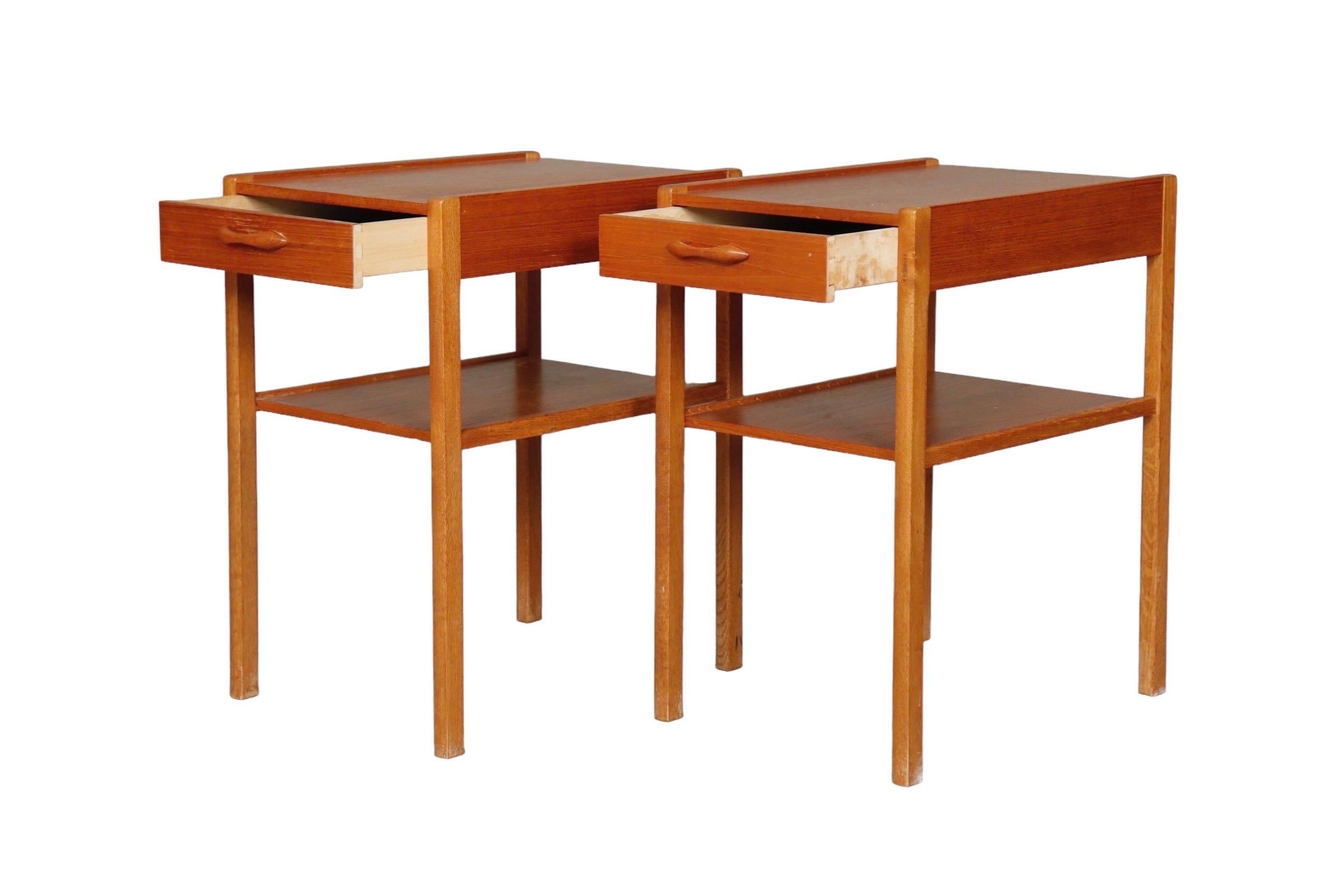 A pair of mid century end tables or night stands made of teak. Each has a single dovetailed drawer that opens with a carved bar handle. Straight legs are supported with a shelf.

Measures: L:12.5”
D:17.25”
H:21.5”.