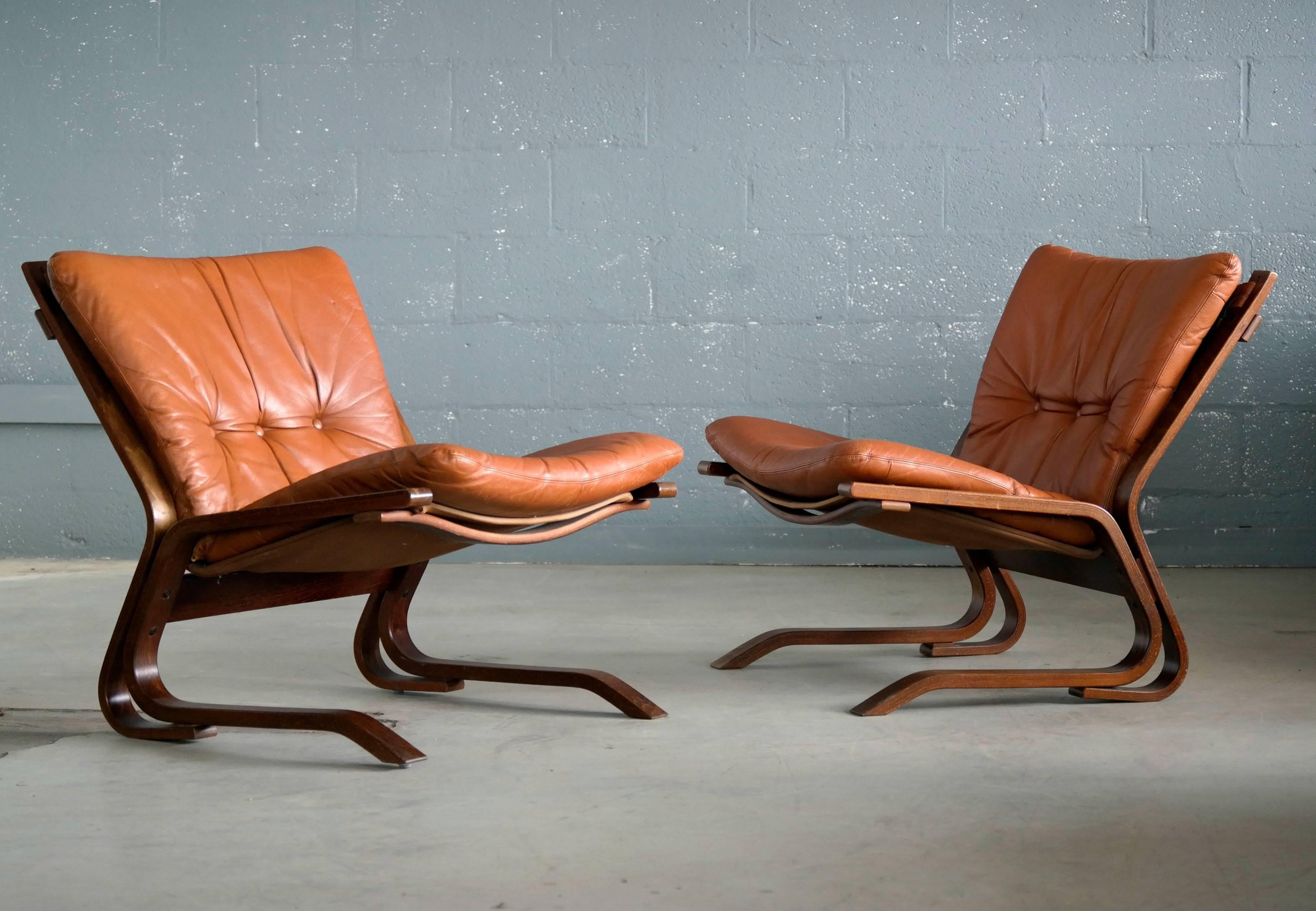 Beautiful pair of easy chairs in rosewood stained laminated beechwood with cognac colored cushions in a canvas sling designed circa 1967 by Oddvin Rykken of Norway and produced early 1970s by Rykken and Co. While similar to the popular designs by