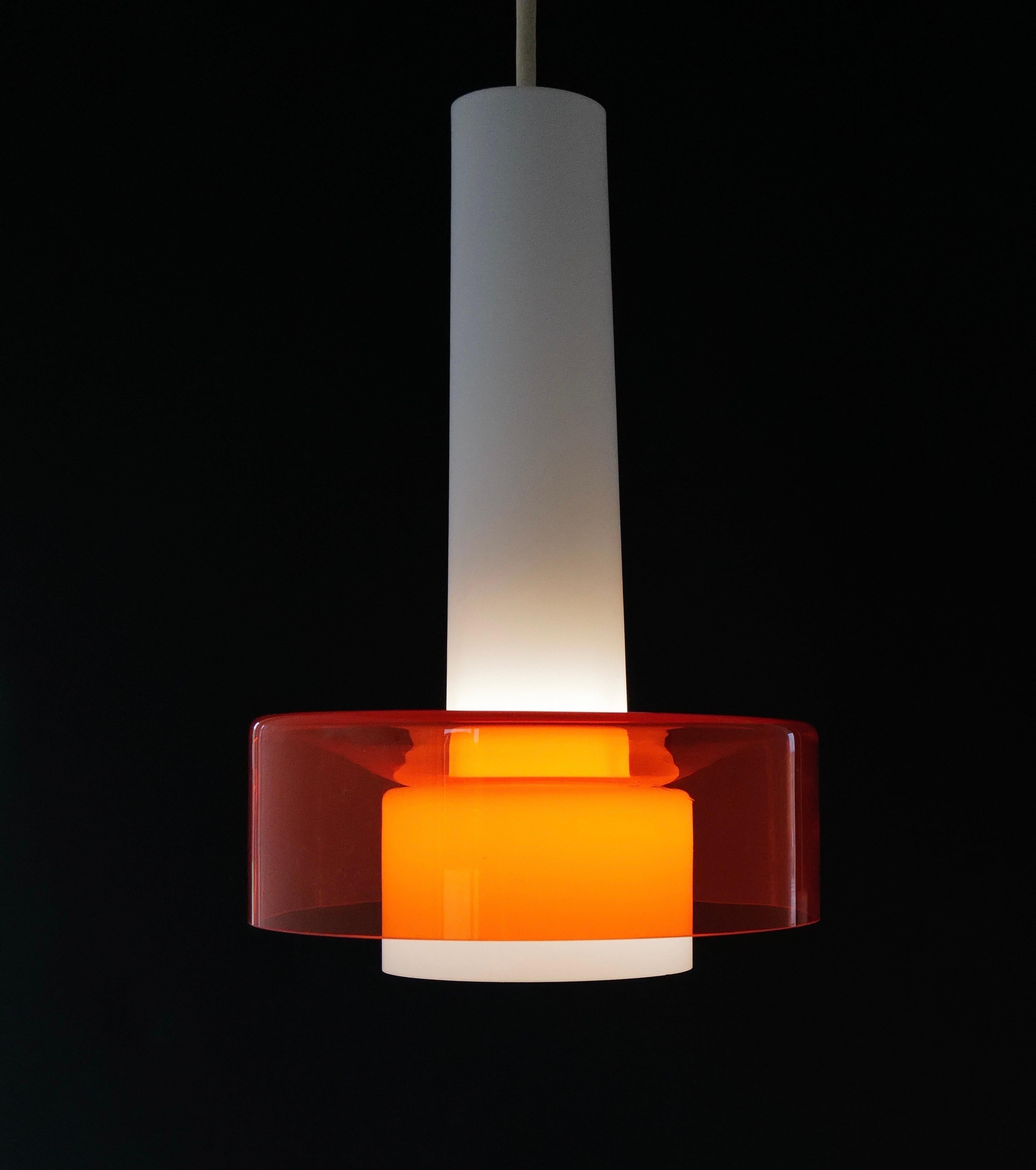 
Striking pair of mid-century pendant lights featuring elongated white opaline glass cones paired with bold, transparent orange glass disc shades. These sculptural fixtures cast a warm, ambient glow and make a vibrant statement in any