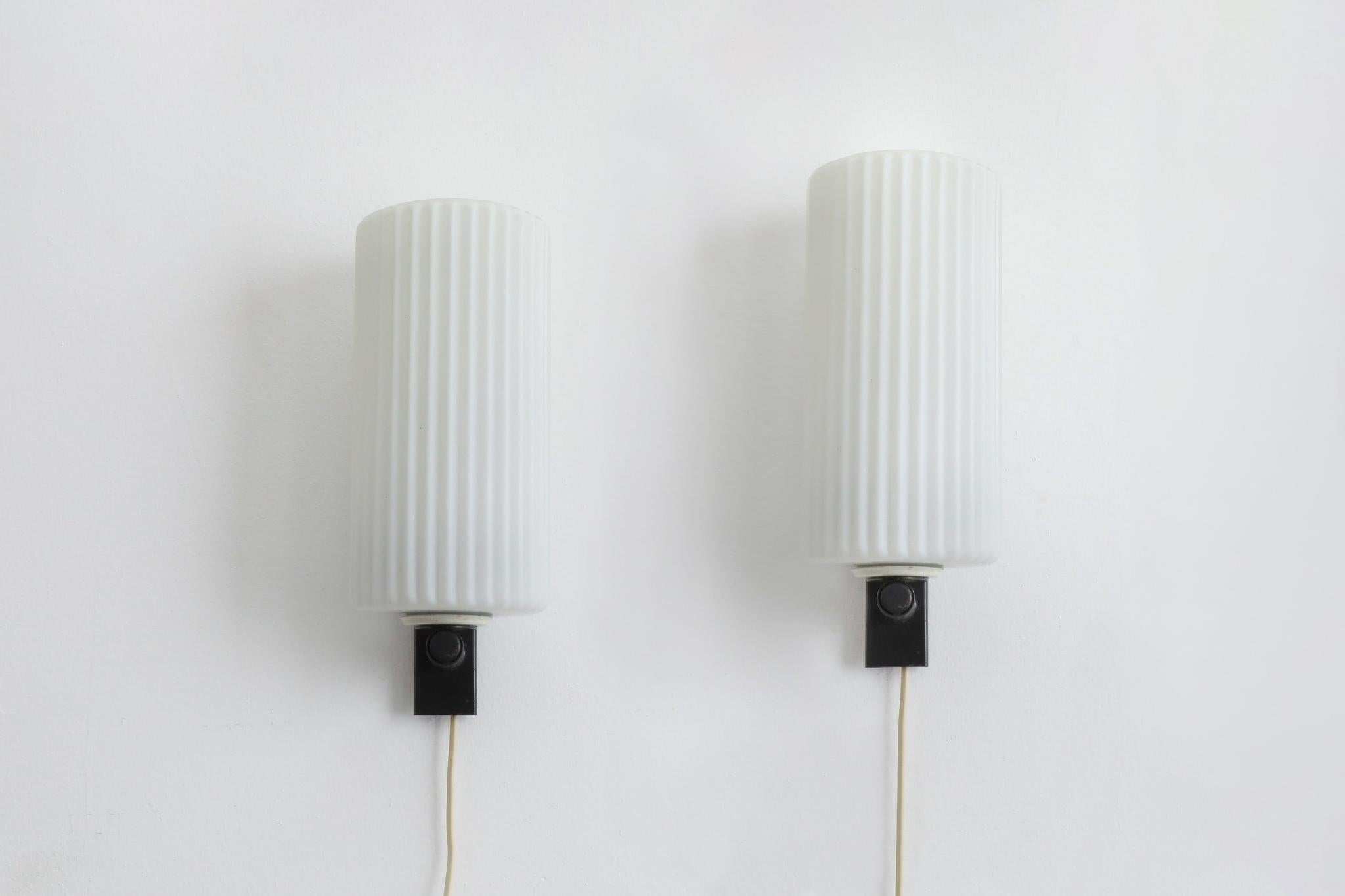 Pair of vintage, Mid-Century, wall mounted milk glass sconces by Dutch manufacturer Philips. Lights have a black enameled metal base that seats ribbed milk glass cylinder shades. Both sconces are in original condition with some visible wear