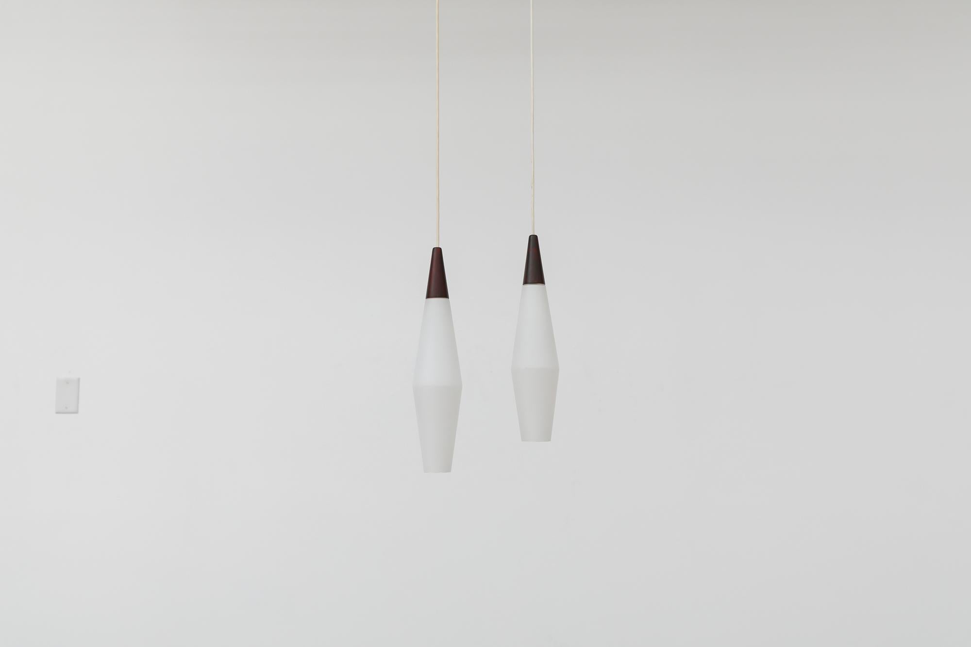 Pair of Mid-Century, Louis Kalff attributed, Philips manufactured, frosted opaline milk glass pendant lights with faux rosewood tops. In original condition with visible wear consistent with their age and use.