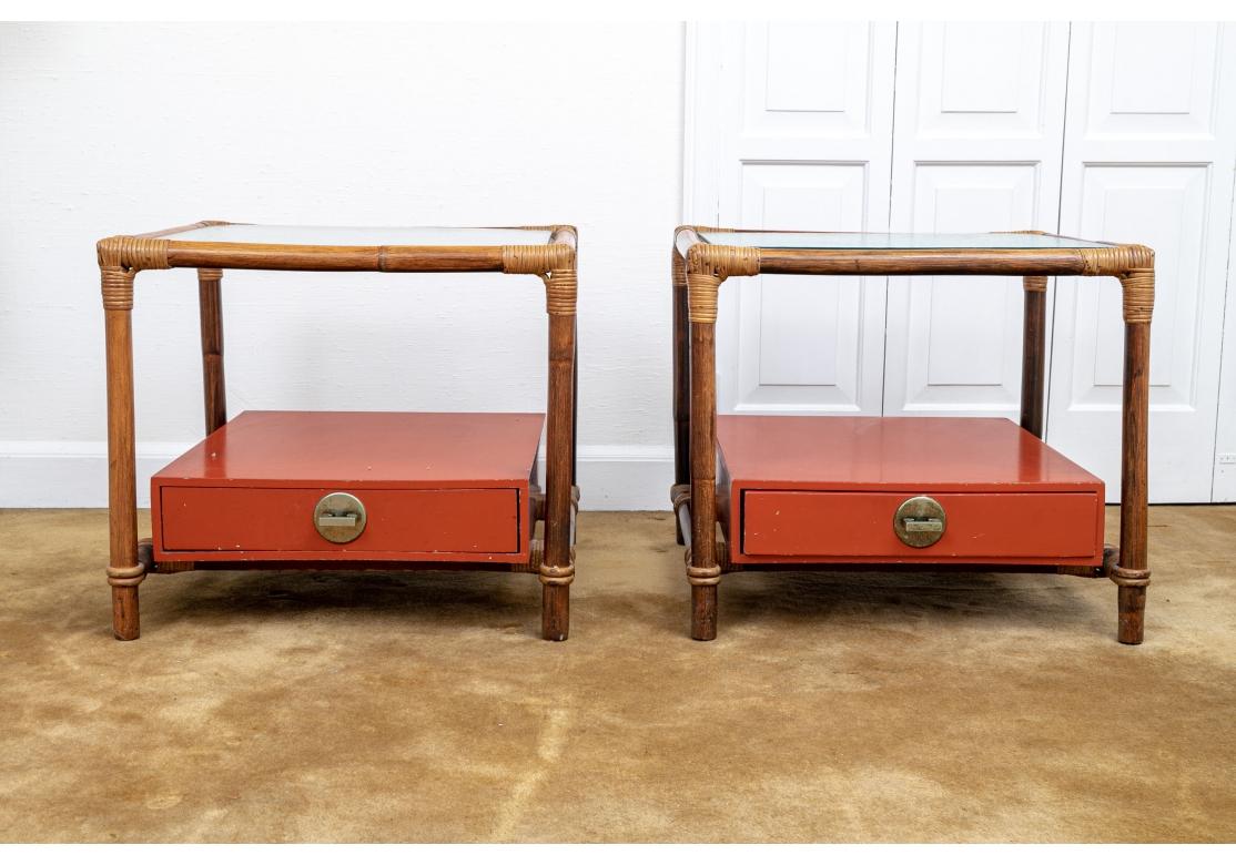 Pair of mid century modern end tables comprised of rattan frames with a Cinnabar color wooden drawer box surmounted on the lower tier, split rattan bindings to joinery and covered with textured glass top  The red box pulls out for storage and