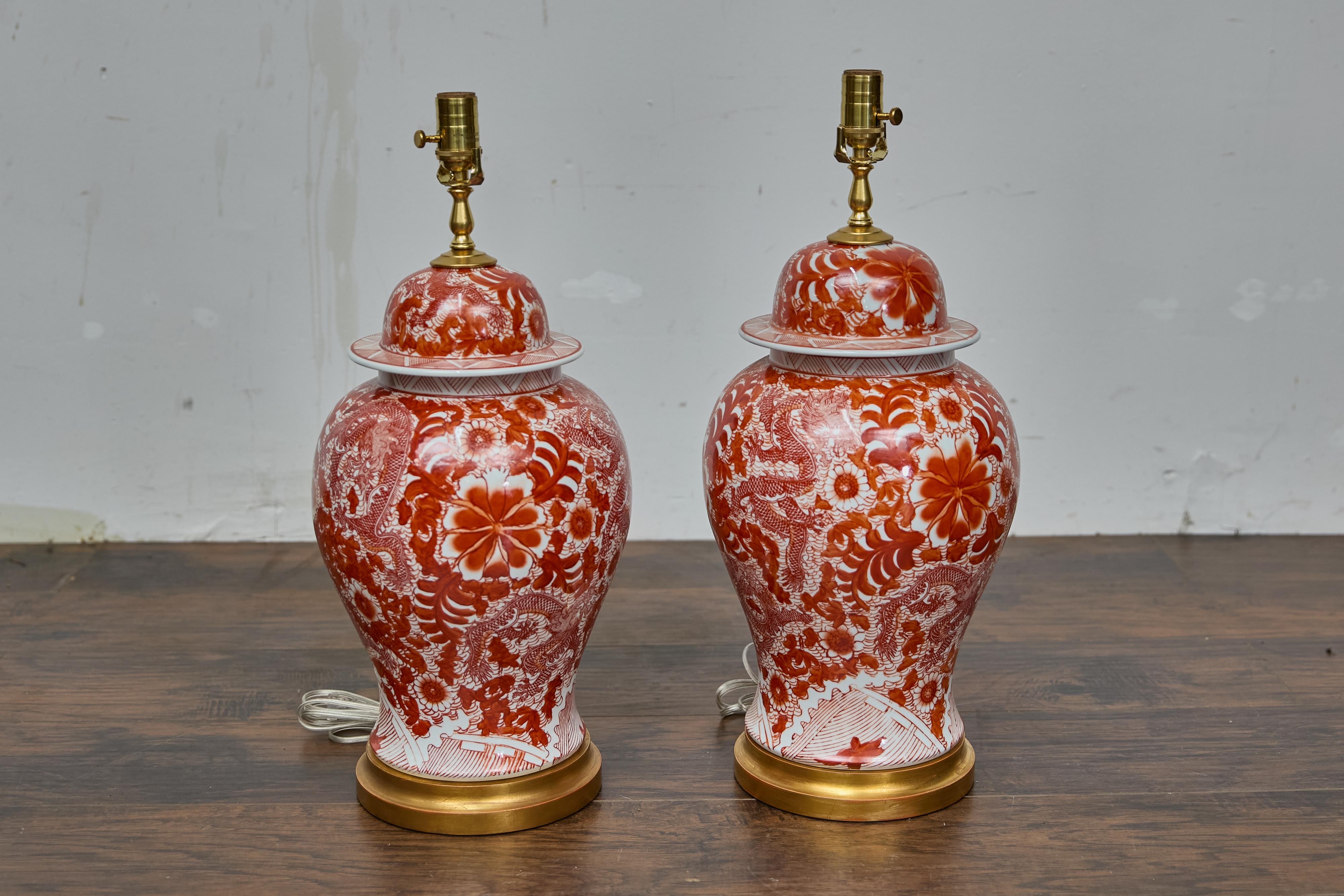 Une vibrante paire de lampes de table en porcelaine rouge et blanche de type temple jars et câblées pour une utilisation aux Etats-Unis. Avec leurs silhouettes imposantes et leurs surfaces richement détaillées, ces lampes apportent énergie et
