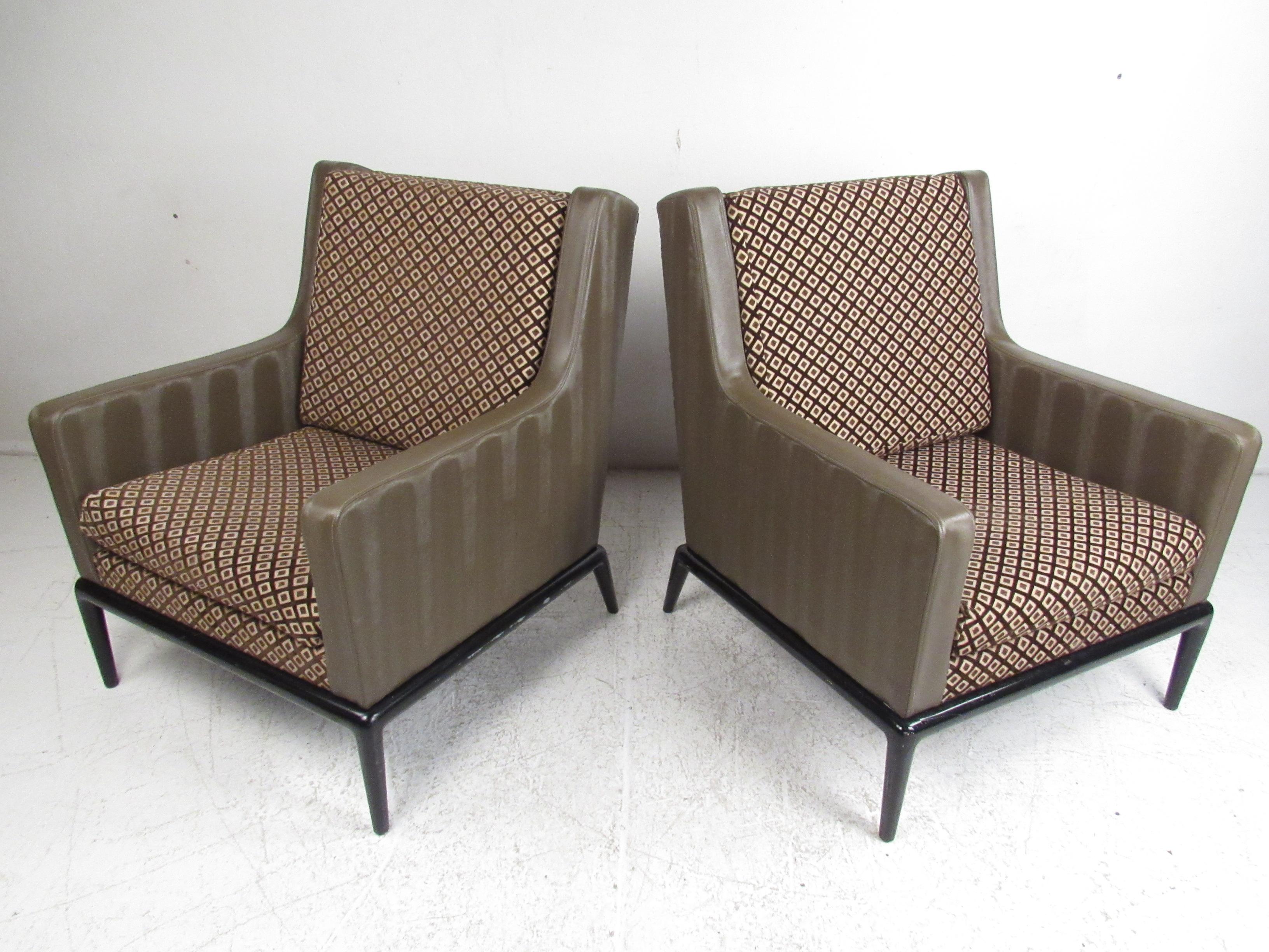 This oversized pair of vintage modern lounge chairs feature a two-tone design with green vinyl and decorative fabric. An attractive pair of arm chairs with removable cushions and tapered legs. The stylish ebonized base and elaborate upholstery show