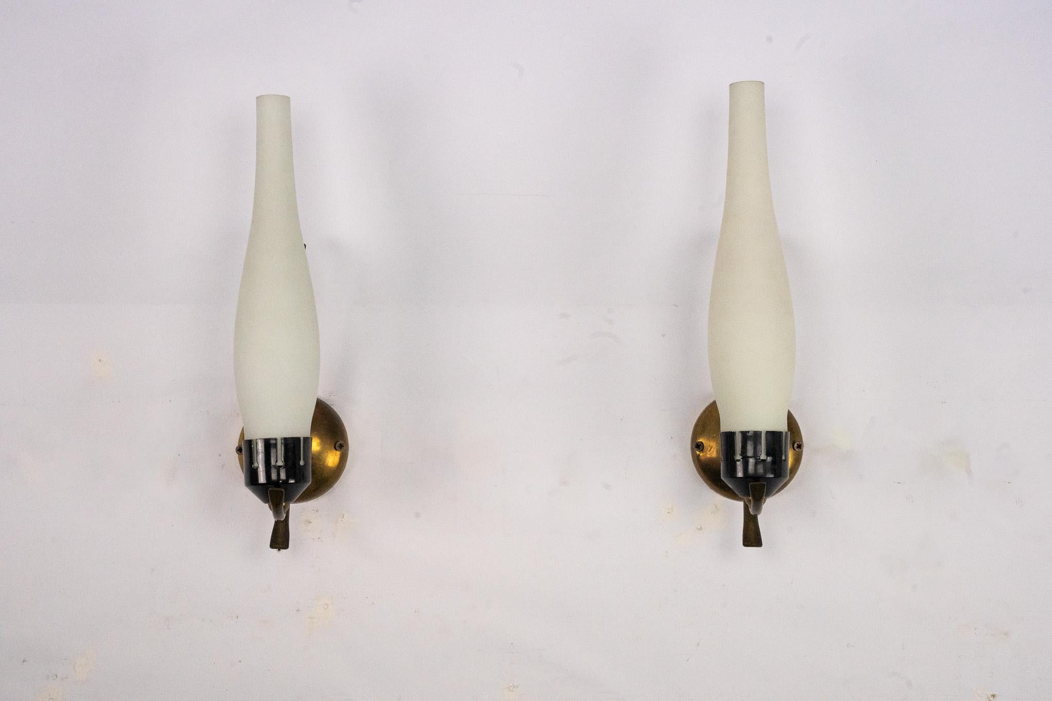 Elegant pair of Italian Mid-Century sconces, attributed to the style of Arredoluce, circa 1950s. Each sconce features a sculptural brass structure with curved detailing, supporting elongated opaline glass shades that diffuse the light with a soft