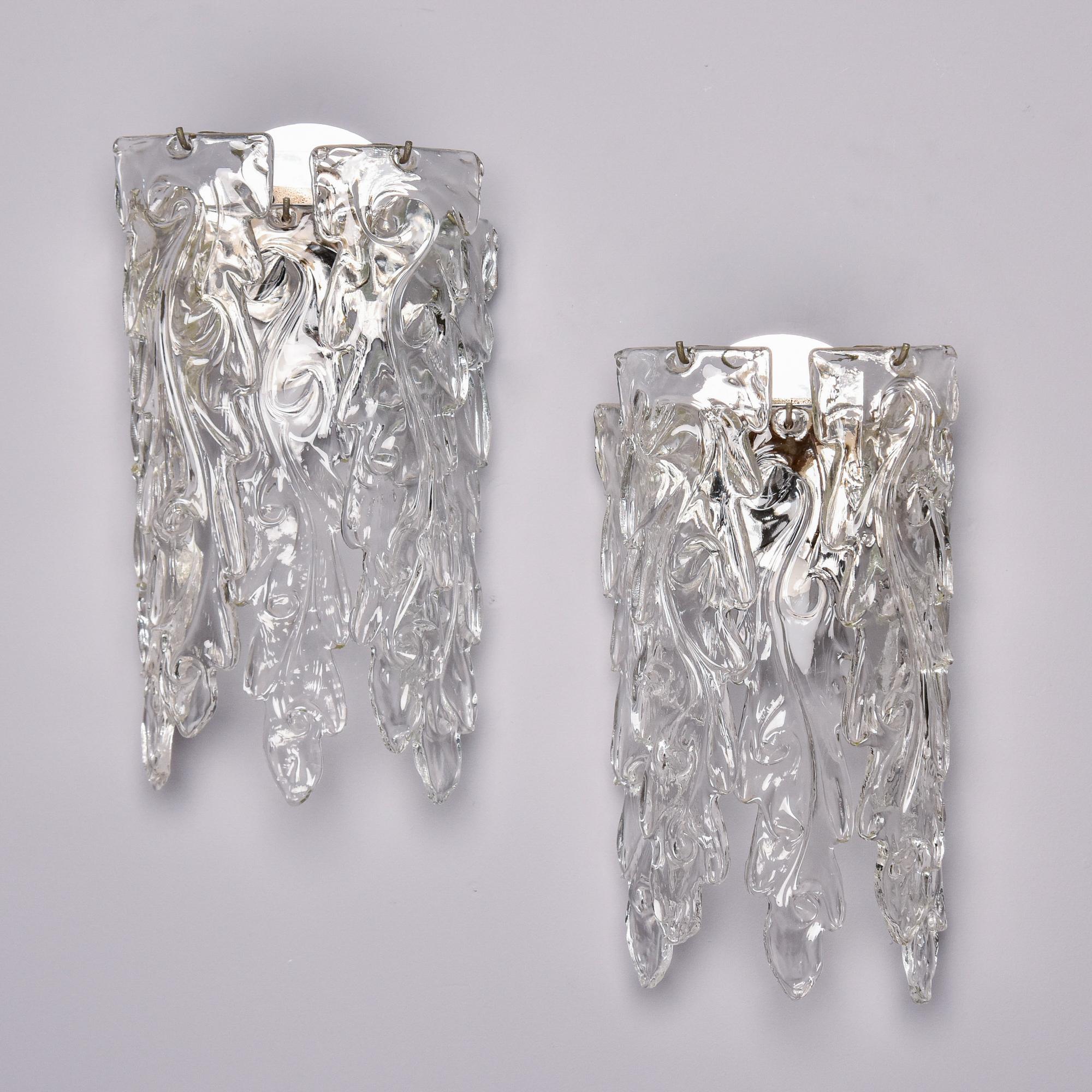 Found in Italy, this pair of Barovier-attributed Murano glass sconces date from approximately 1970. Each sconce has one internal candelabra-sized socket and four, heavy clear textured glass pendants that surround the socket and are suspenced from a