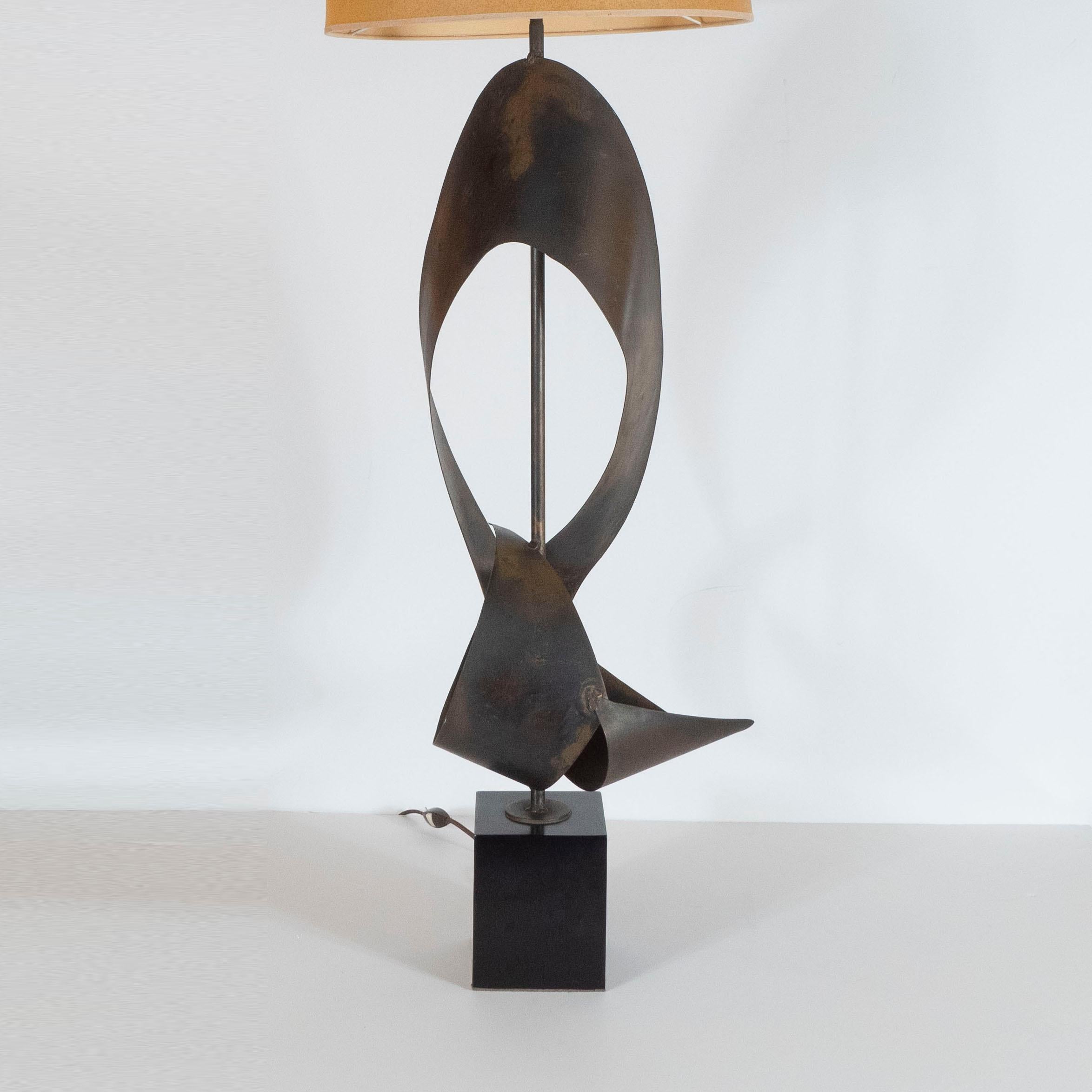 This dramatic and graphic pair of table lamps were realized in the United States, circa 1960. They feature contorting ribbons of patinated steel threaded with a cylindrical rod in the same material that attaches to a volumetric square black enamel