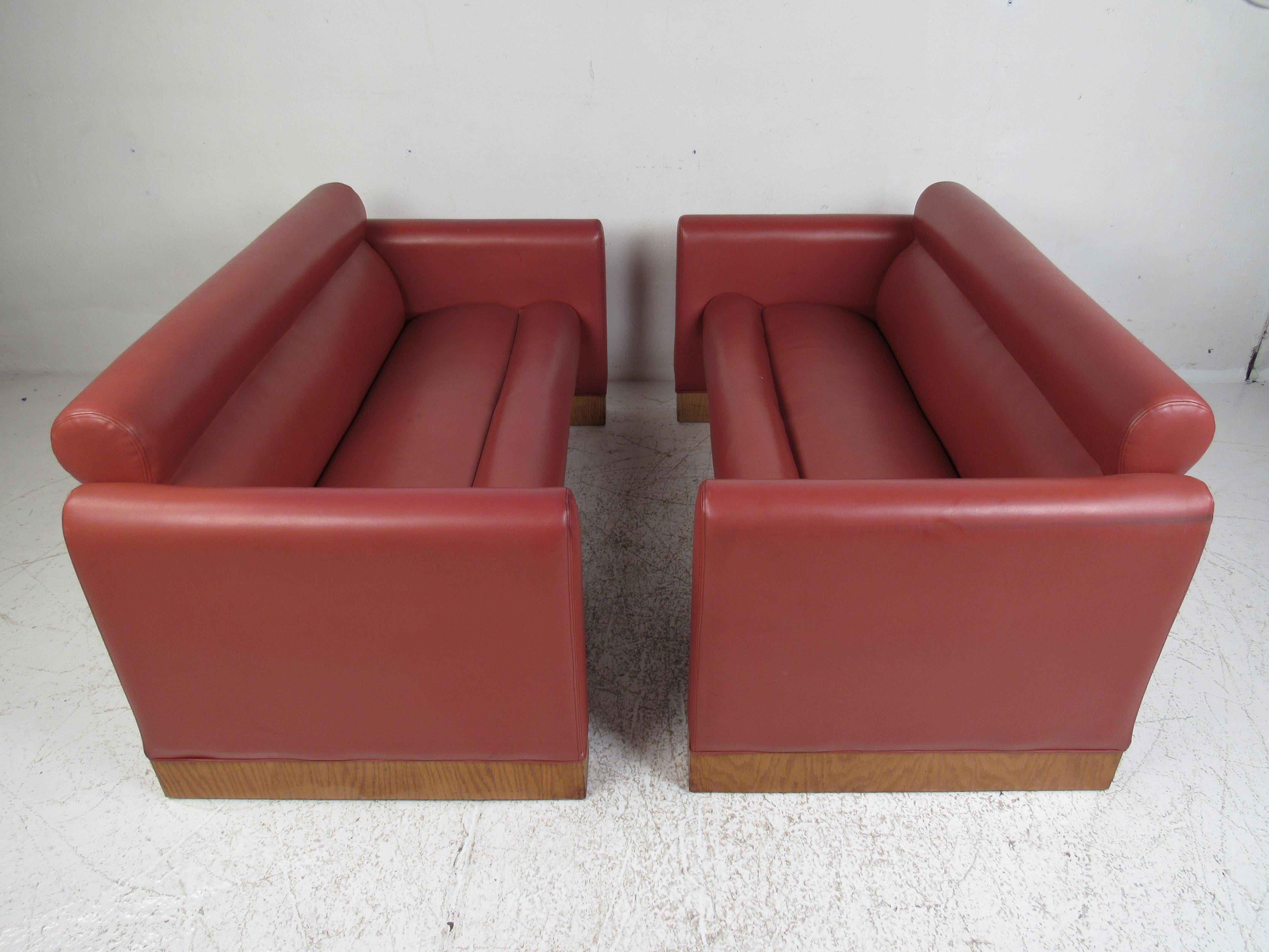This beautiful vintage modern pair of sofas feature pink vinyl upholstery and a base with wood trim. A sleek and comfortable design that makes a statement in any seating arrangement. Please confirm item location (NY or NJ).