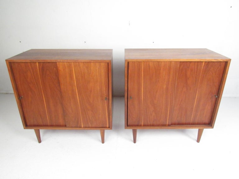 This stunning pair of vintage modern cabinets feature conical metal pulls on each sliding cabinet door. A compact design that provides ample room for storage within its large compartment with a shelf. A well made pair with a vintage walnut finish,