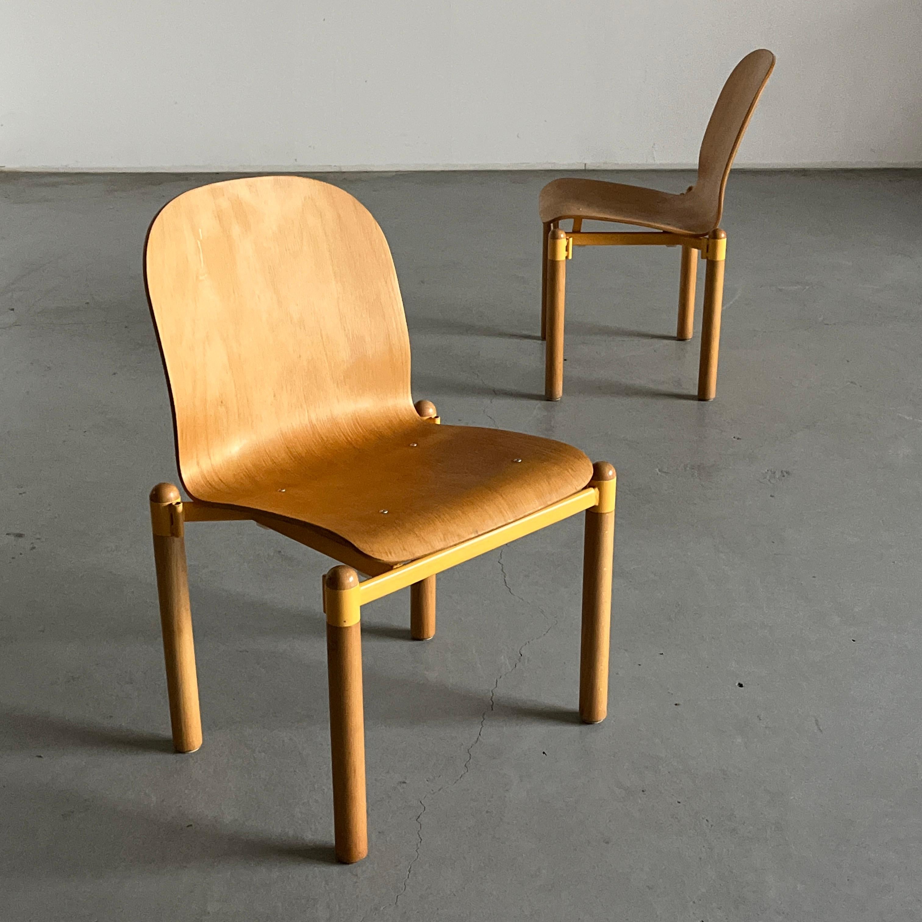 An example of Mid-century modern production and craftsmanship, the chairs feature a bent plywood seat and backrest with a glossy natural wood finish, with a new matching yellow upholstery. Supported by four legs interconnected via a yellow metal