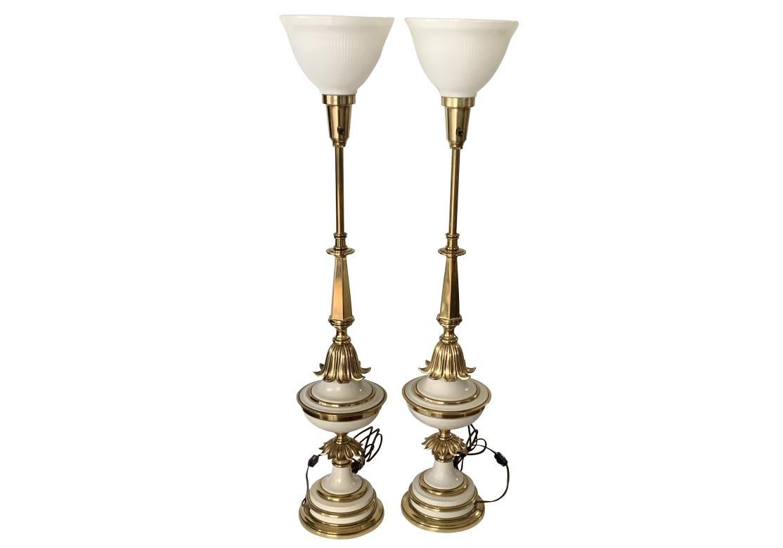 Pair of mid century torchiere table lamps by Stiffel in brass with white enameling. The lamps with white glass shades with reeded raised design and embossed Stiffel as shown. The footed lamps with alternating panels of white enameling and brass, the