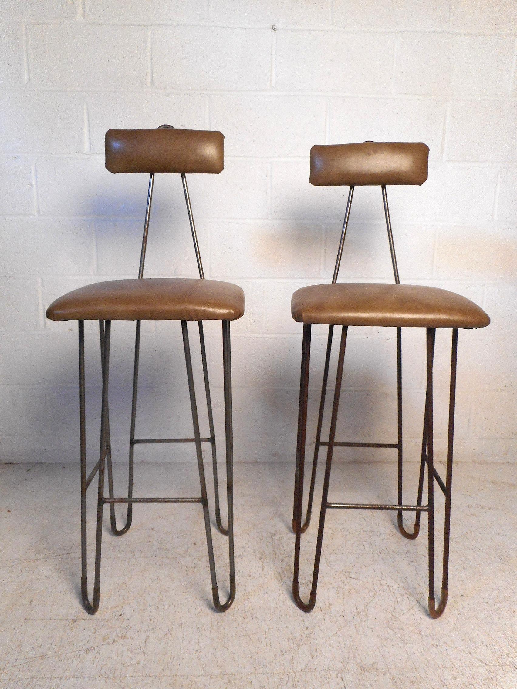 These stylish and unusual mid-century stools feature sturdy iron hairpin frames, comfortable seating, and sleek faux-leather upholstery. Angular backrest supports peak above the cushion giving the stools an interesting look. A great addition to any