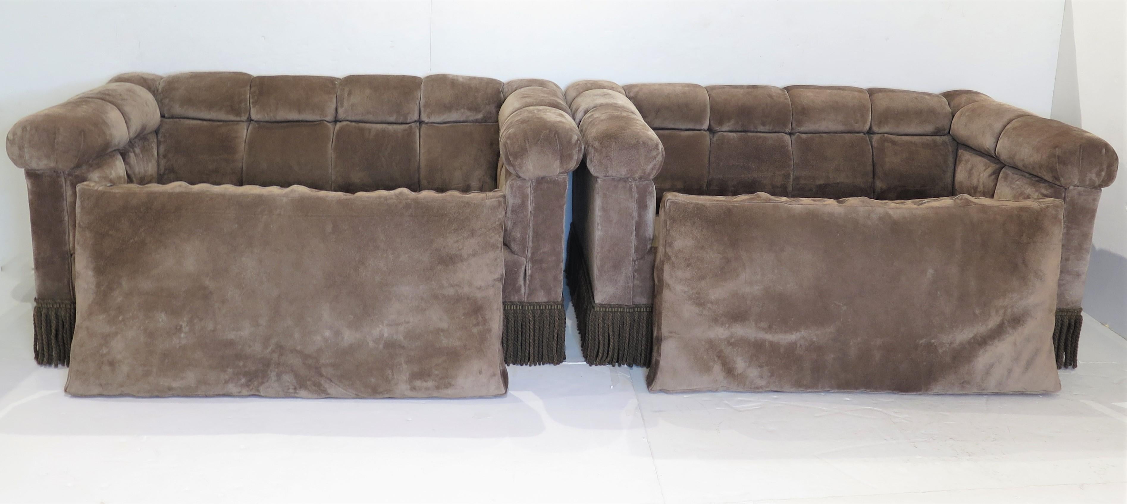 pair of mid-century modern Dunbar Chesterfield sofas with brown suede button tufted upholstery and bullion fringe, single seat cushion, early 1960s 

the sofas, originally low to the floor, were raised as their owner got older, the bullion fringe