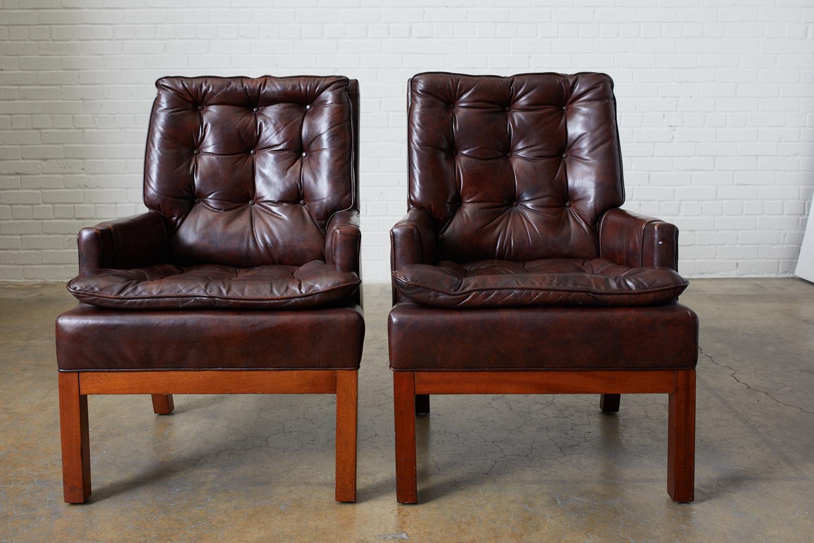 Mid-Century Modern pair of dark chocolate brown tufted library chairs or club chairs. Upholstered in a bonded tufted leather with a parson style wood leg. Very comfortable with soft tufted cushions.