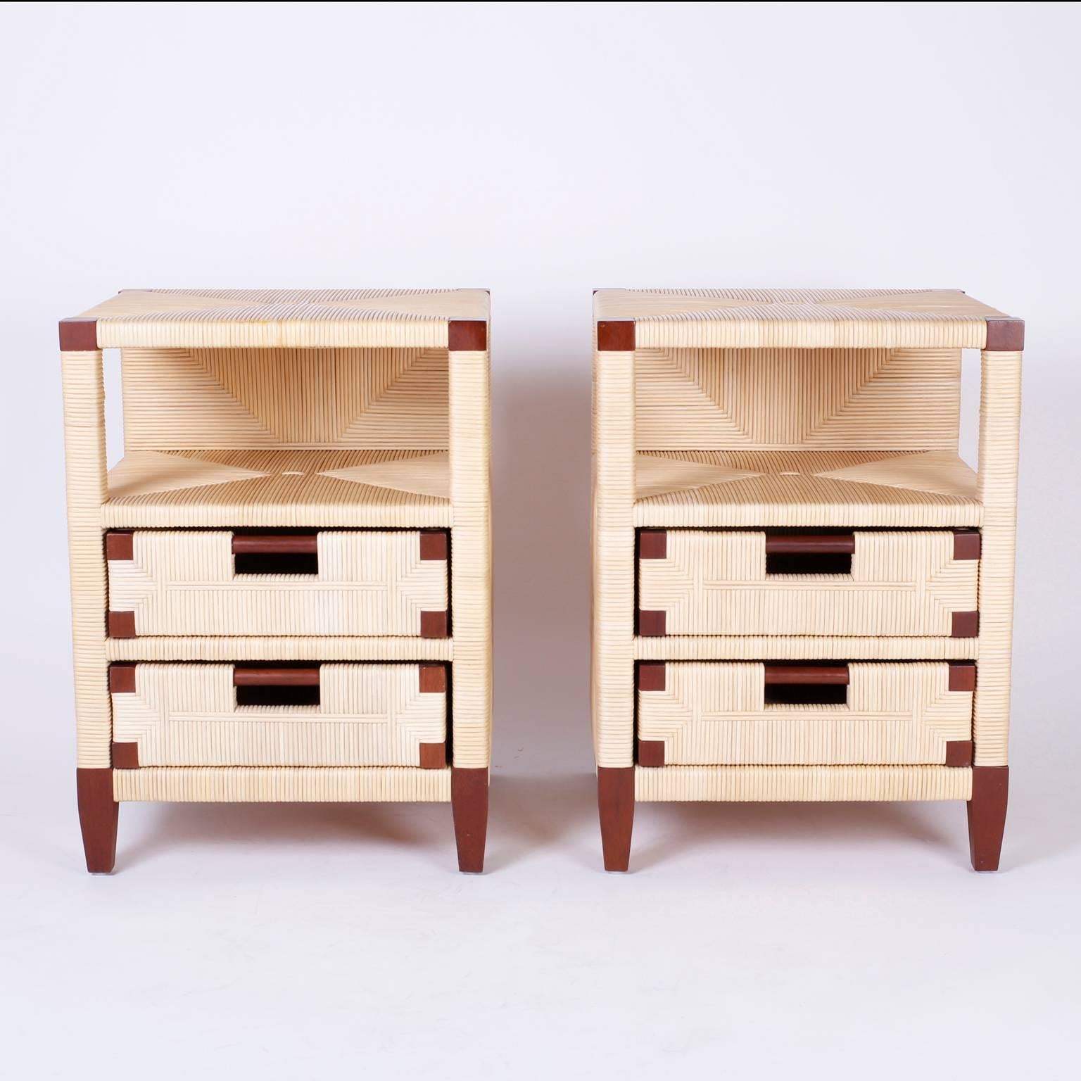 Handsome pair of nightstands with two drawers and book storage constructed with mahogany wrapped in geometric patterned reed. Having tapered legs and finished on the back Merbau collection designed by John Hutton. Branded Donghia on the bottom.