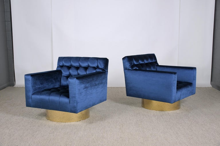 A wonderful pair of upholstered swivel lounge chairs handcrafted and professionally reupholstered in blue velvet fabric with a tufted biscuit design by our team of expert craftsmen. The vintage pair of club chairs have new medium-firm foam inserts