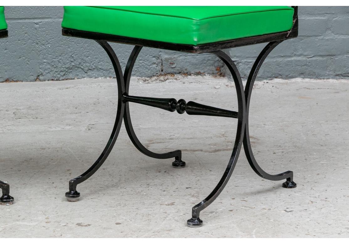 A Pair of vibrant Green Vinyl side chairs after Tommi Parzinger. Iron frames in black paint with spindle lower backs and brass finials on the support tops. Raised on elegant pair of double curved legs with flat feet and a shaped stretcher. The upper