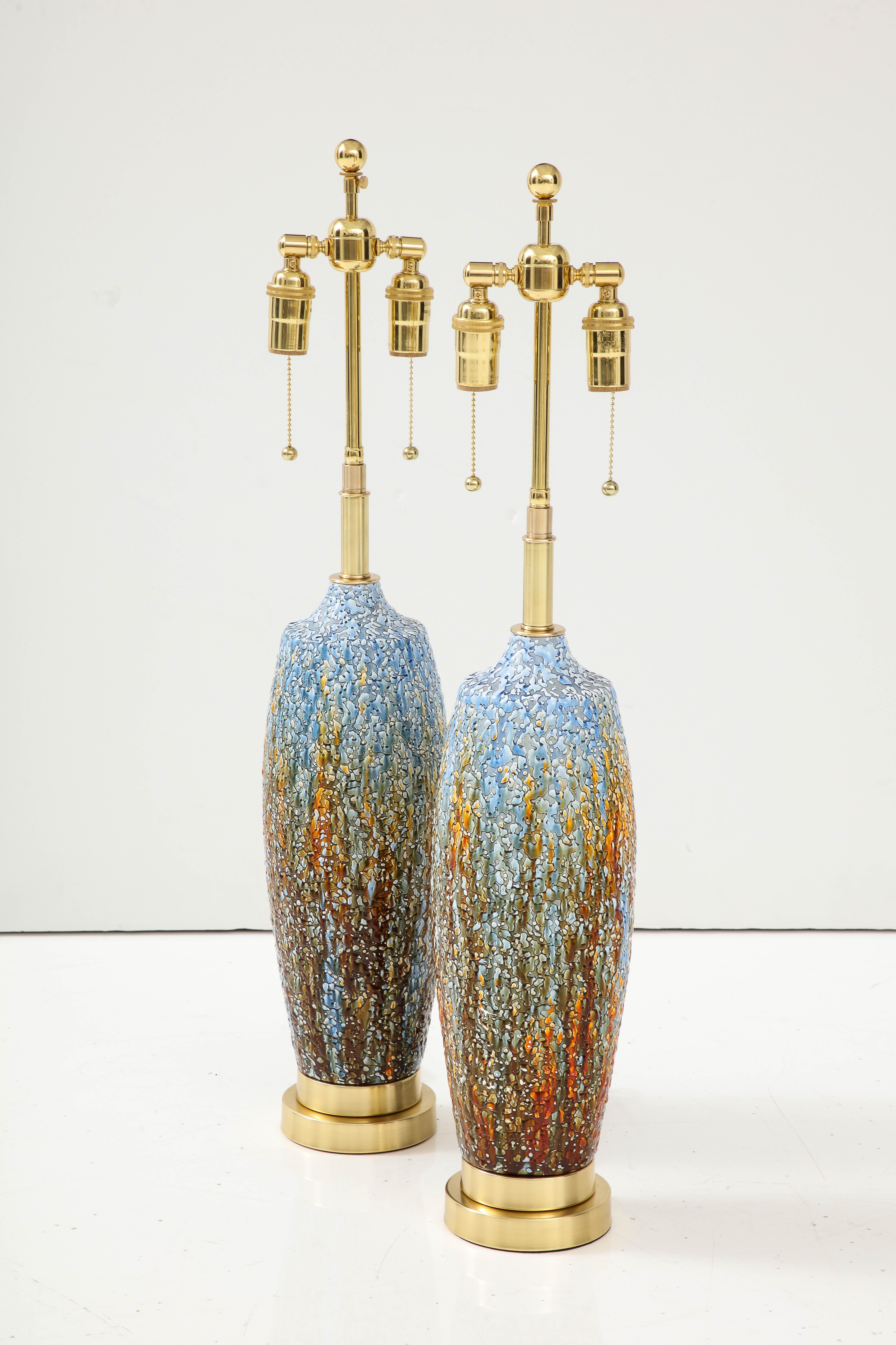 Pair of Mid-Century Modern ceramic lamps with a textured volcanic glazed finish.
The lamps have been Newly rewired with adjustable polished brass double clusters and silk rayon cords. Each socket is 60 Watts / 120 Watts per lamp.
The height to the