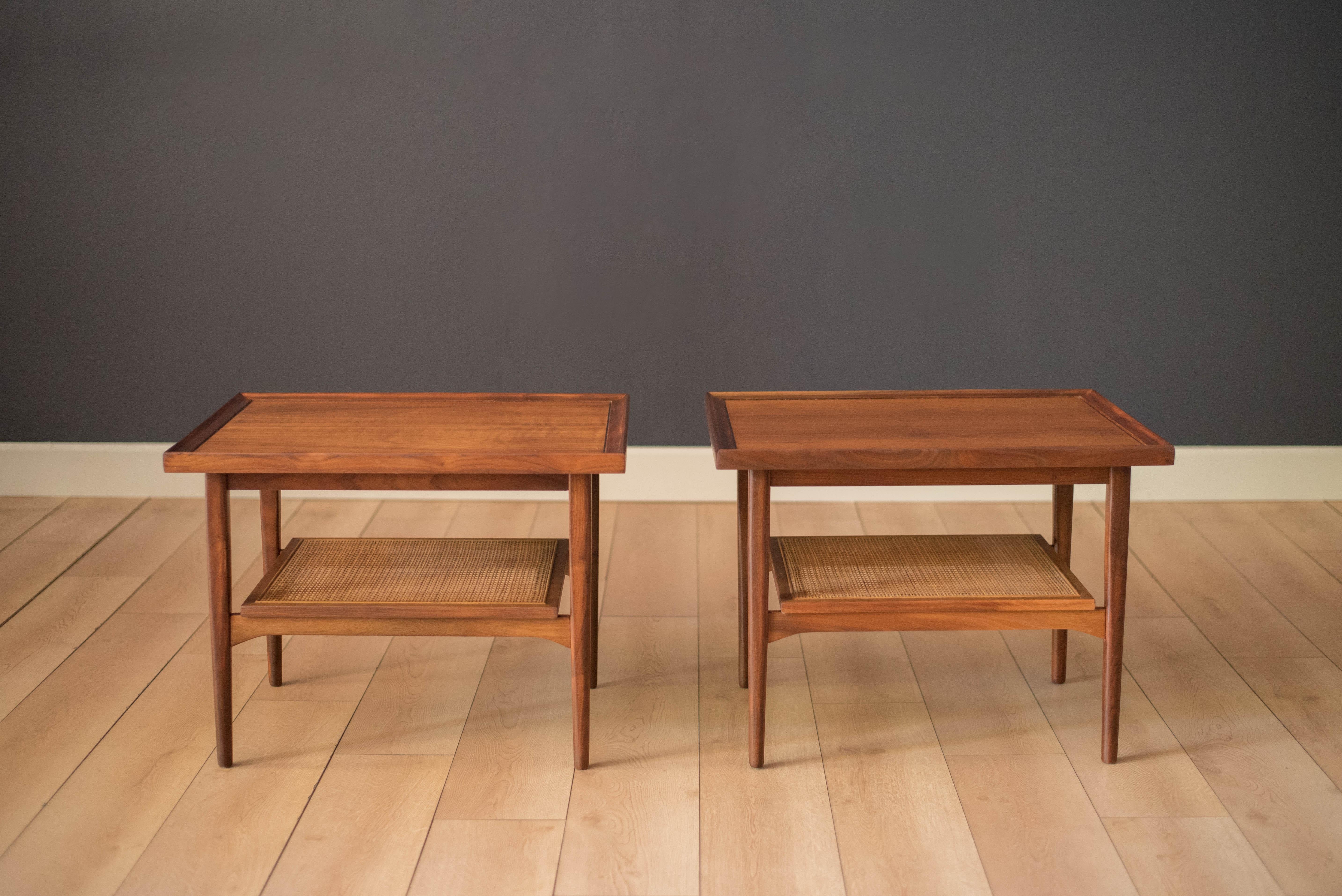 Vintage set of walnut side tables from the Declaration collection designed by Kipp Stewart & Stewart McDougall for Drexel Furniture Co. This pair features a raised edge table top supported by tapered legs. Offers a lower caned magazine shelf for