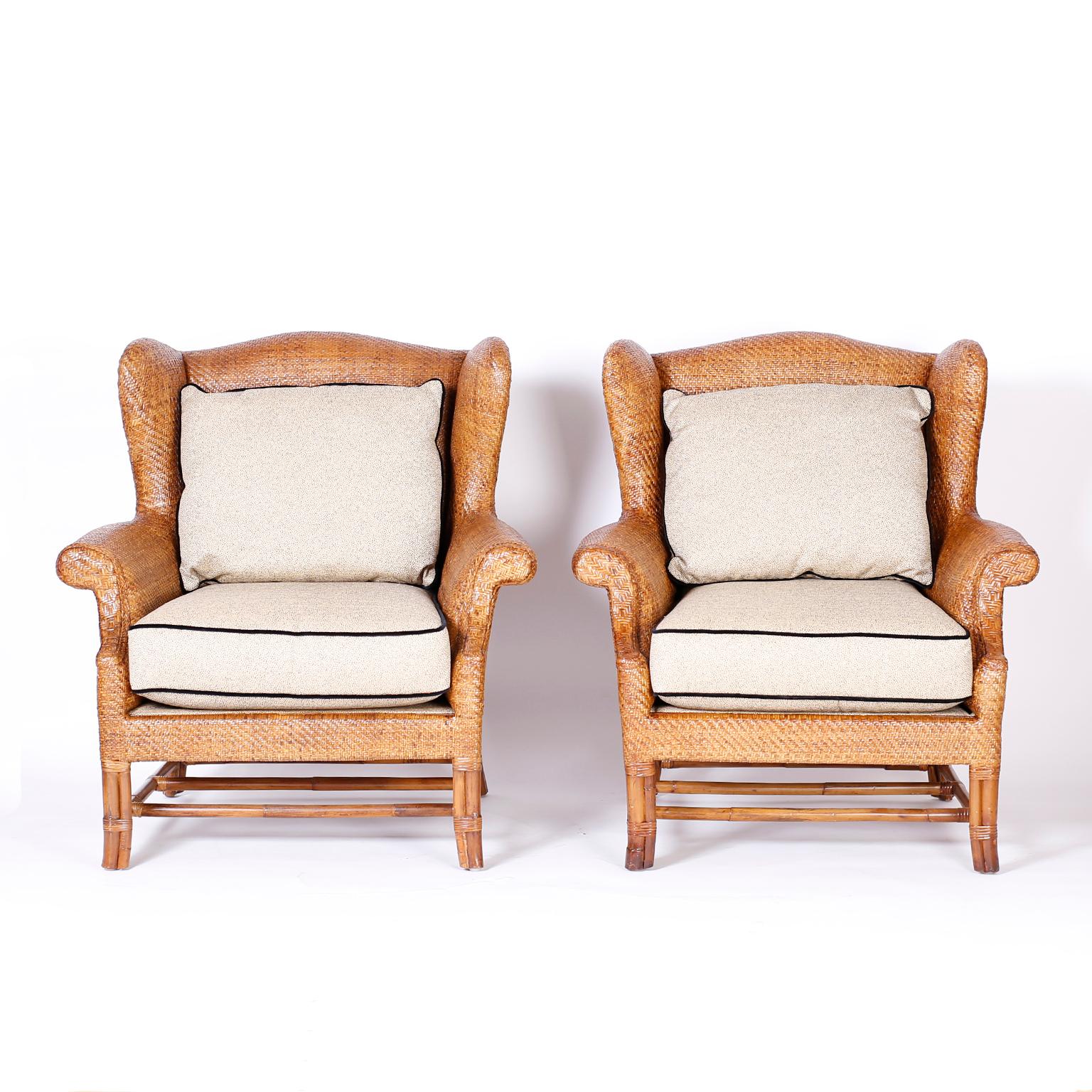 Impressive pair of wingback armchairs with a Classic form crafted in wicker or reed in a herringbone pattern. The legs and stretchers are bamboo. Signed Baker on the bottoms.